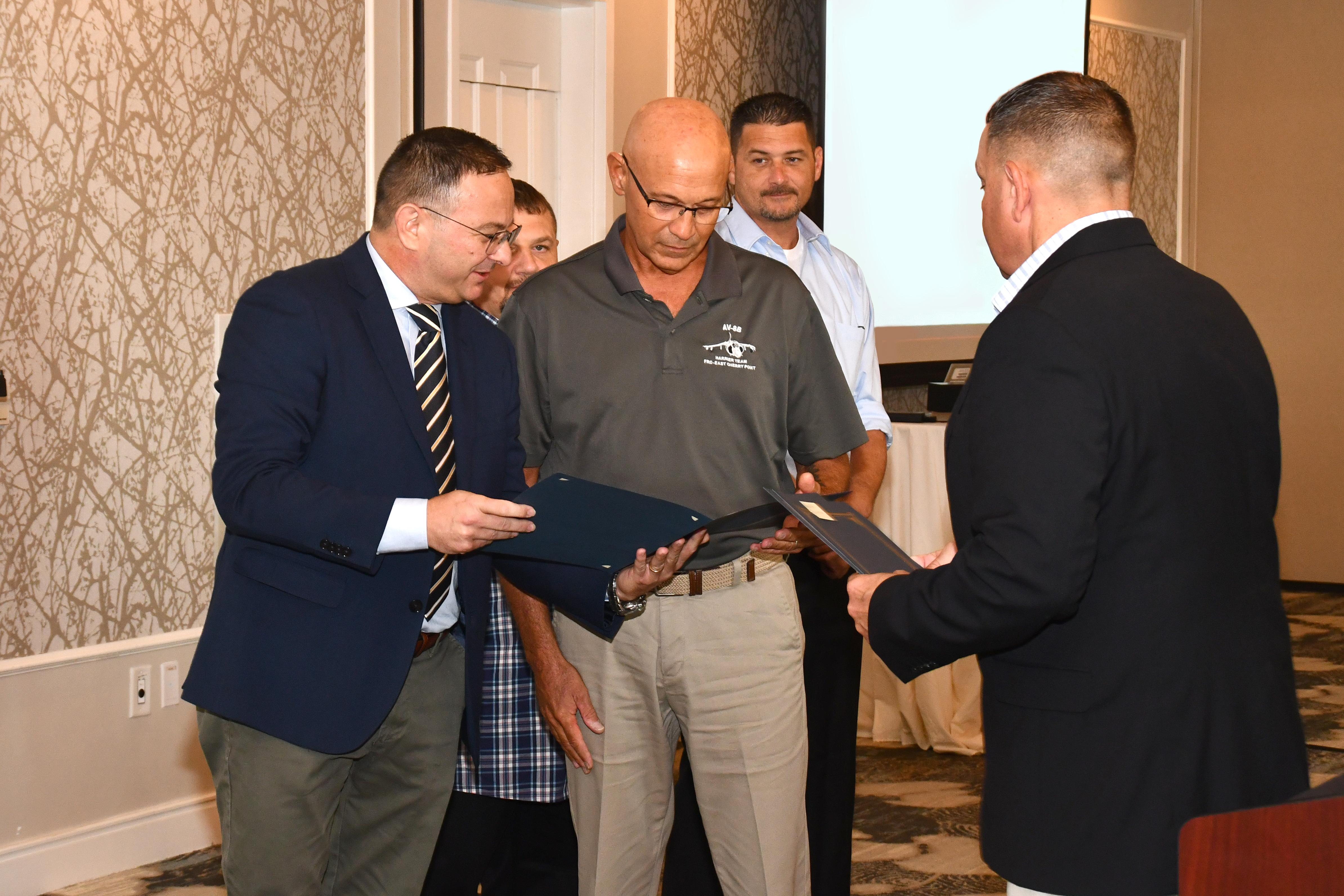 Italian Navy AV-8B Deputy Program Manager Cdr. Sergio D’Agostini, left, presents Fleet Readiness Center East (FRCE) aircraft electrician Eric Ellenberger with a letter of appreciation citing the successful completion of Harrier upgrades performed at Naval Air Station Grottaglie in Italy. Ellenberger was one of six FRCE employees recognized for their support of the Italian AV-8B Harrier fleet.