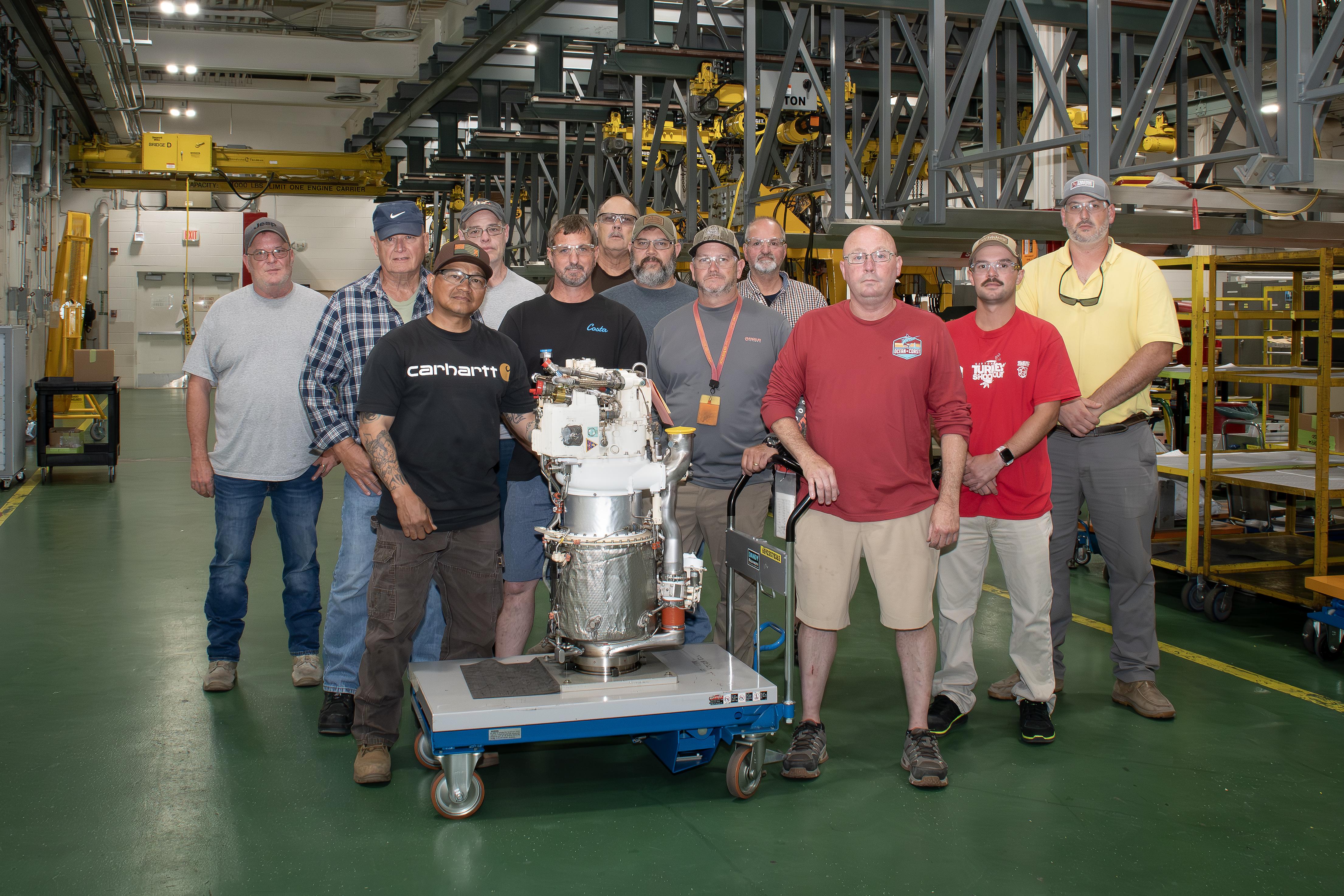 Artisans at Fleet Readiness Center East’s (FRCE) Engine Driven Compressor and Gas Turbine shop stand for a group photo with a freshly overhauled auxiliary power unit for the F/A-18E/F Super Hornet. FRCE recently achieved a significant production milestone by eliminating high-priority backorders for auxiliary power units used in the Super Hornet, bolstering the platform’s mission readiness.