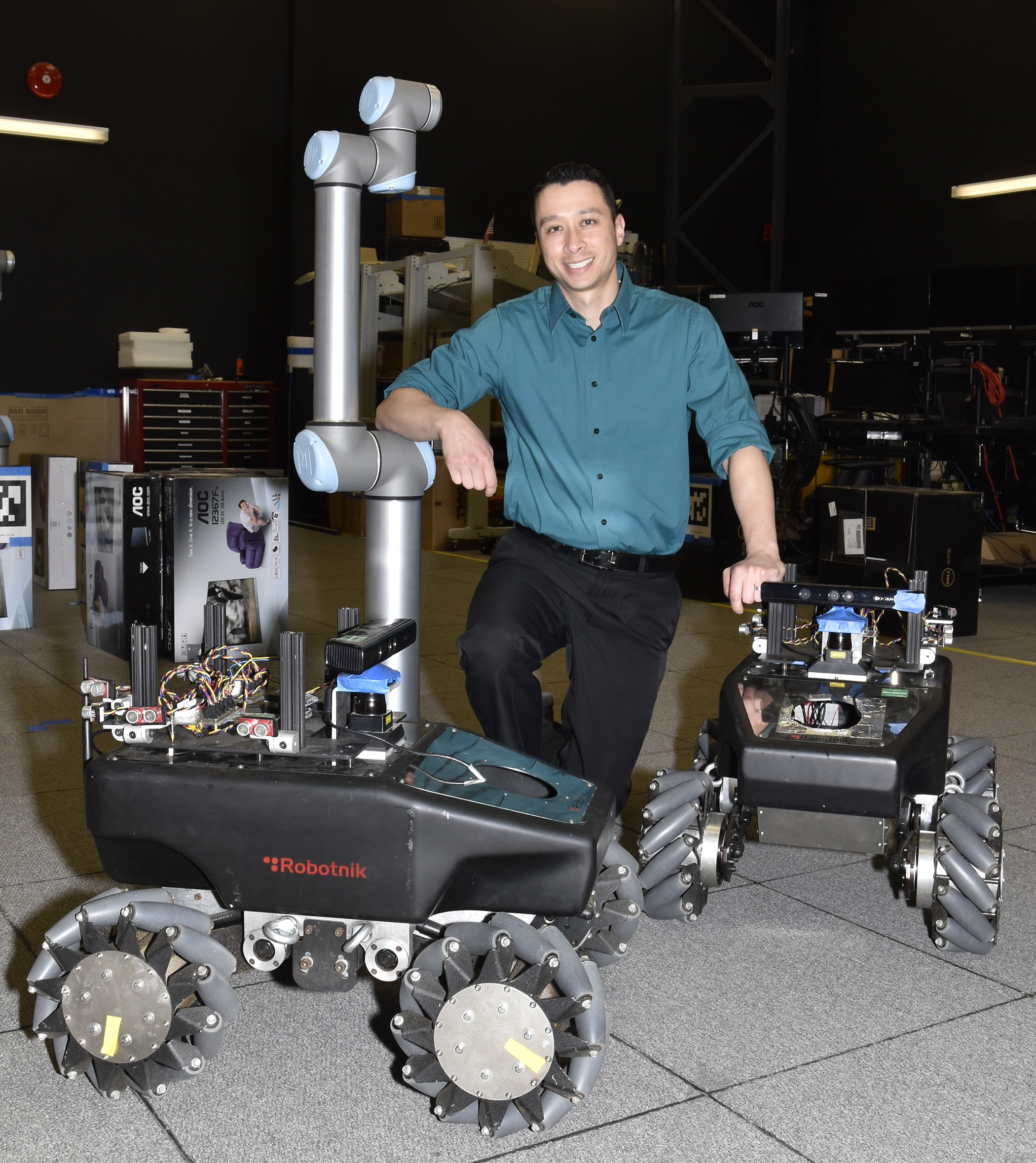 Dr James Hing poses with robots in the Robotics and Intelligent Systems lab