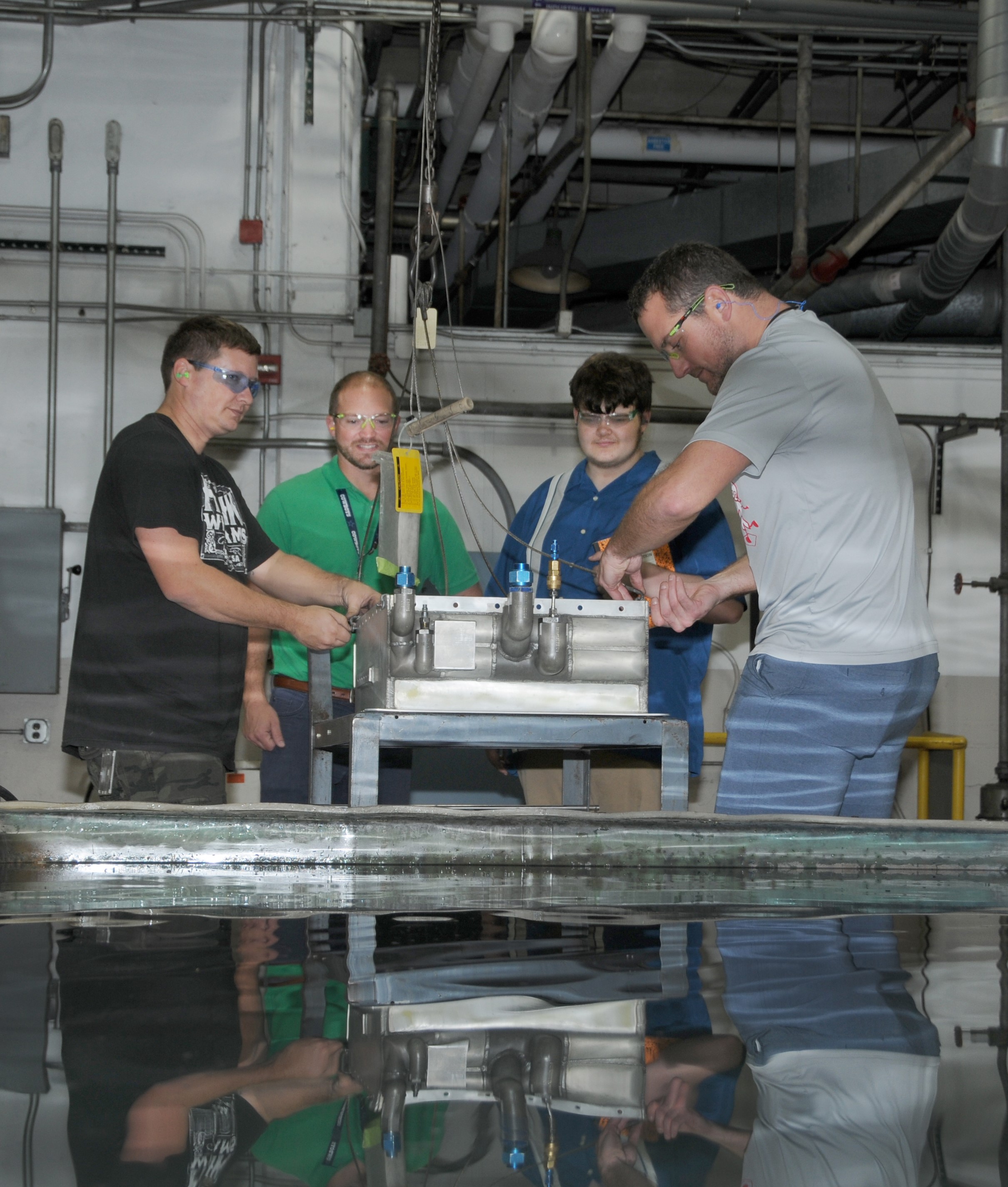 Artisans lower H-53 helicopter radiator into test pool to check for air leaks