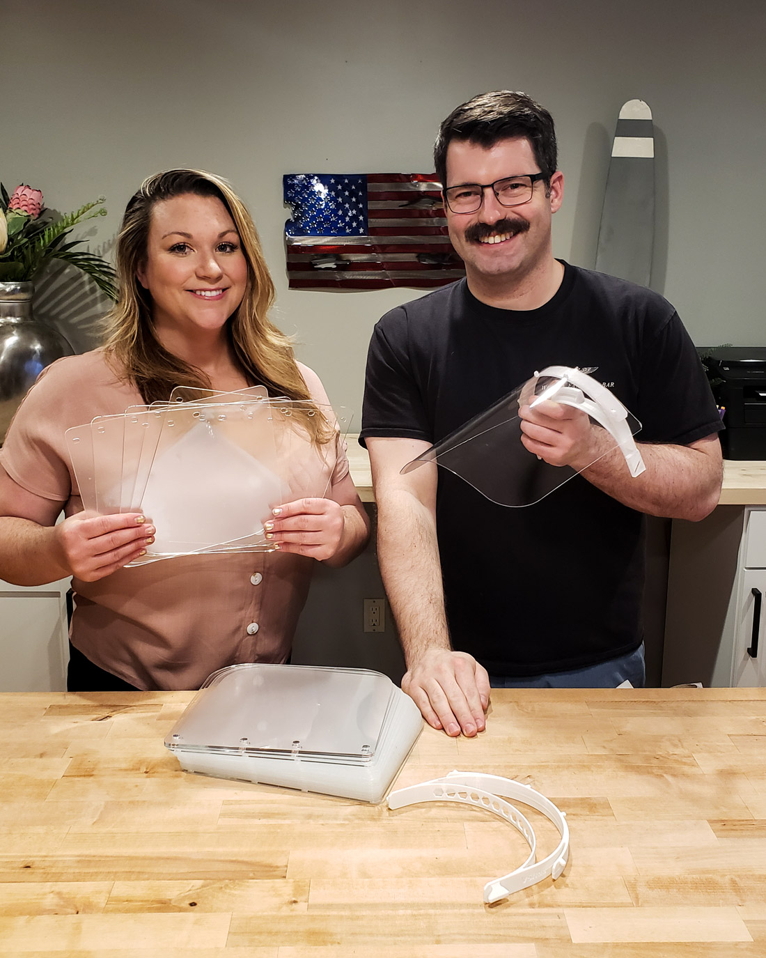 Lt. Gavin “Flanders” Kurey, right, and his wife Katie show some of the hundreds of acrylic face shields they have cut at their metalworking shop for use in making face protection to combat the spread of COVID-19. (U.S. Navy photo by Lt. Gavin Kurey)