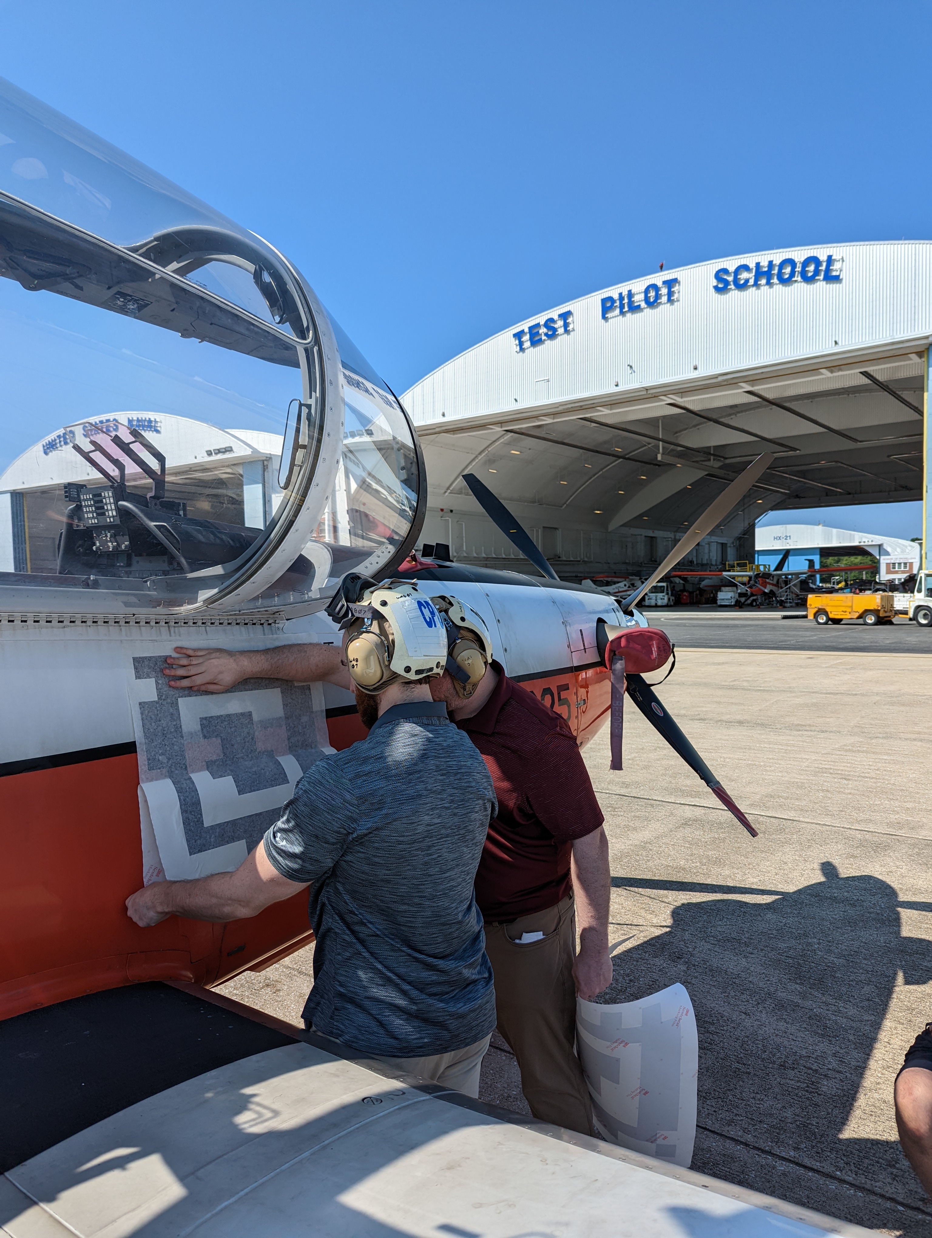 Engineers apply a fiducial tag along the side of a T-6 Texan aircraft in front of a hangar at the U.S. Naval Test Pilot School.