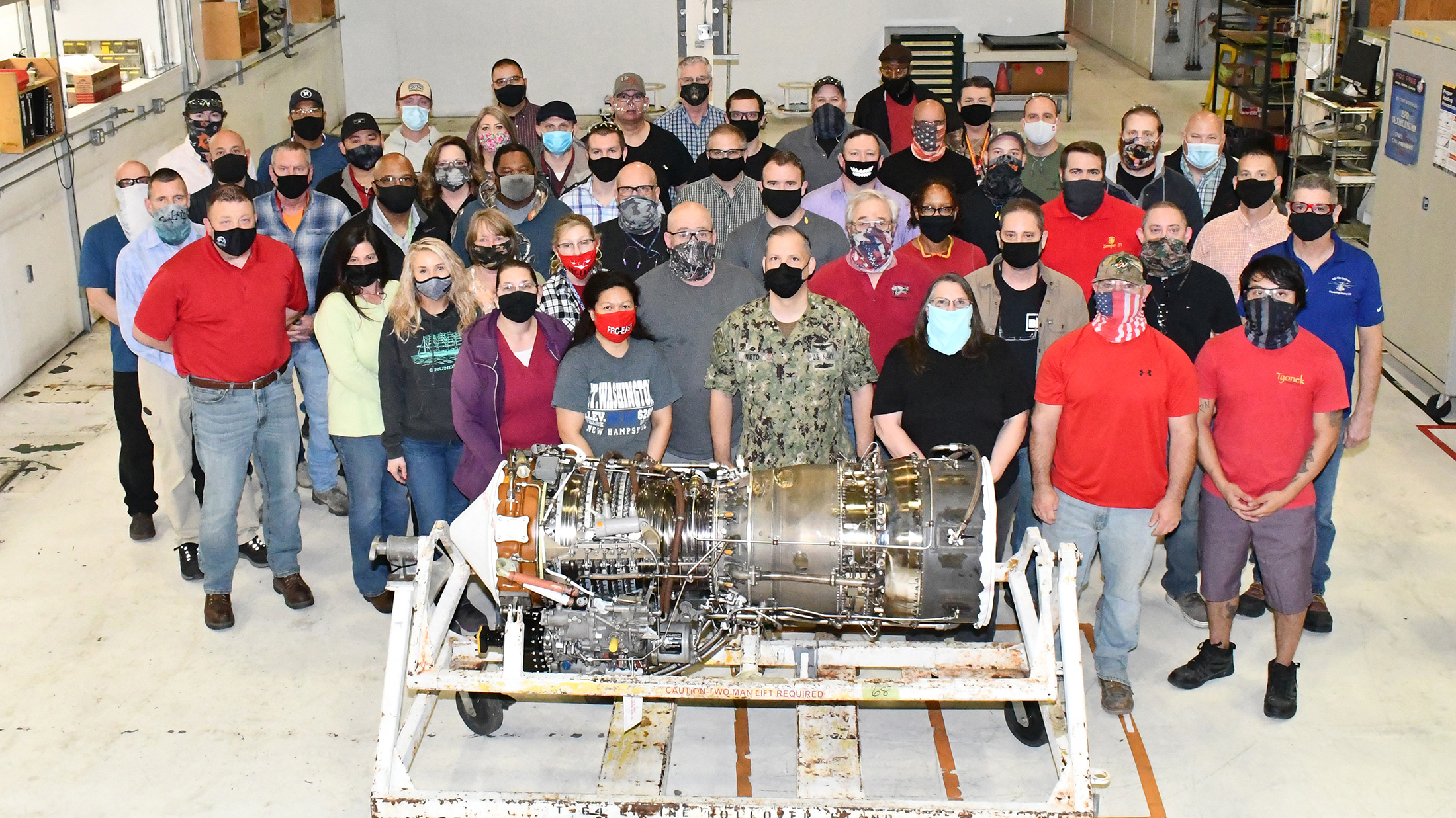 Group of aircraft workers poses for group photo behind T64 engine
