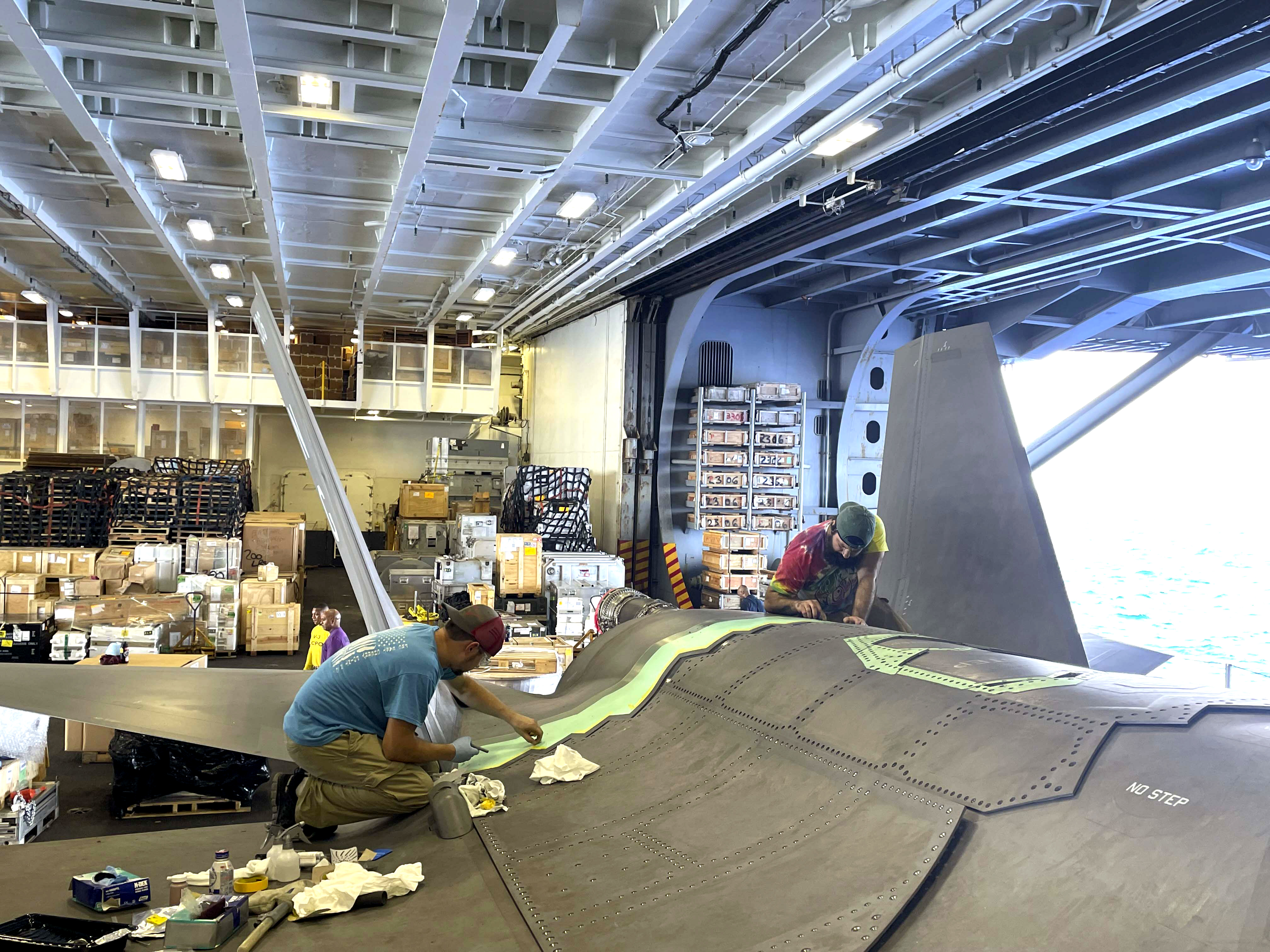 Two men repair F-35C Lightning II aircraft in hangar aboard aircraft carrier