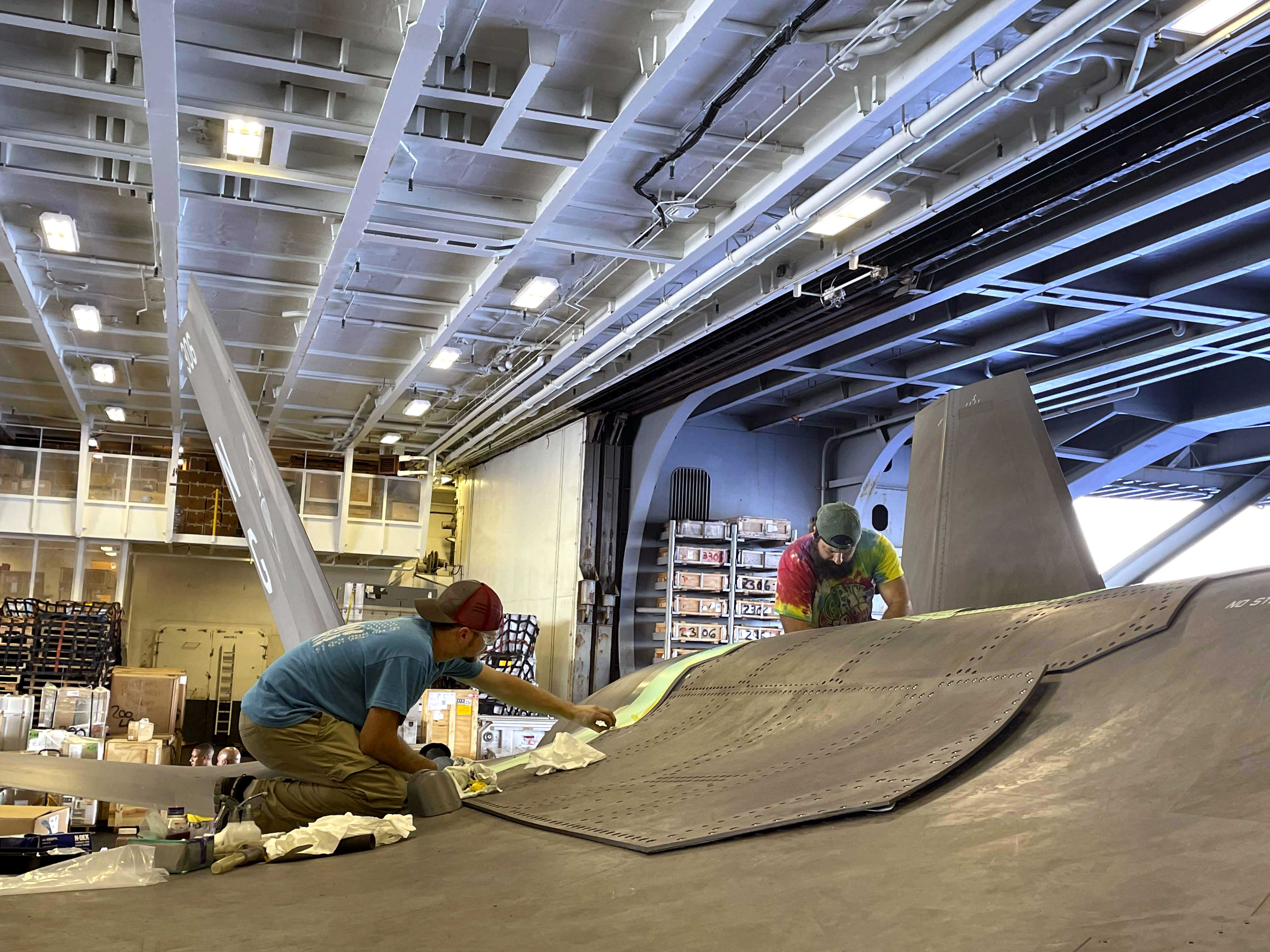 Two men repair F-35C Lightning II in hangar aboard aircraft carrier