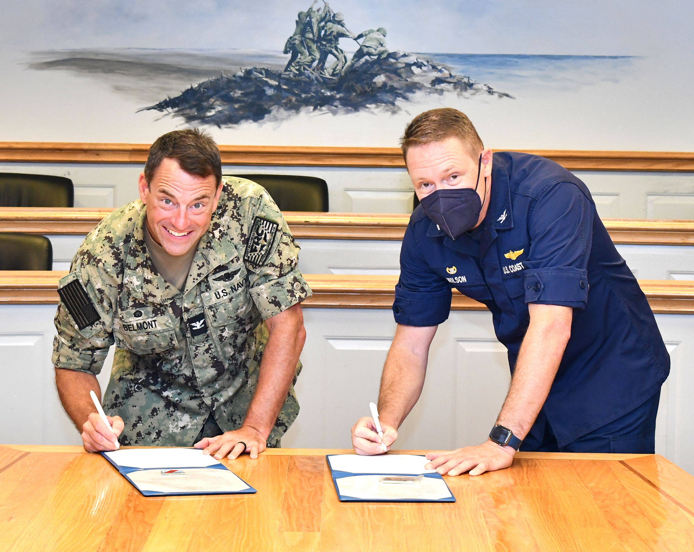 Two commanders look at camera while signing documents