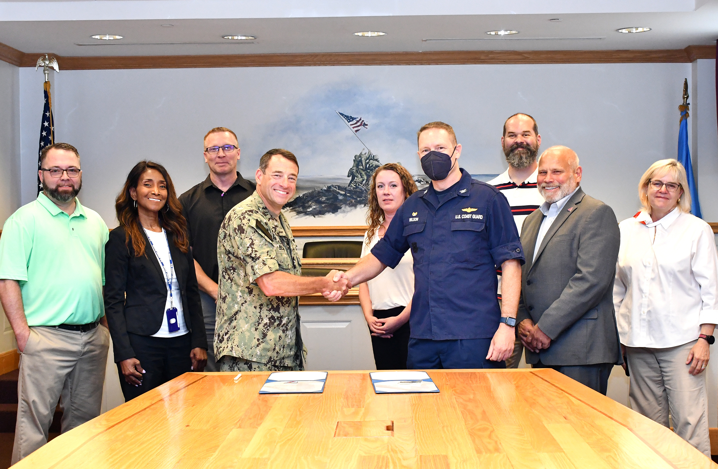 Group poses behind table as two commanders shake hands