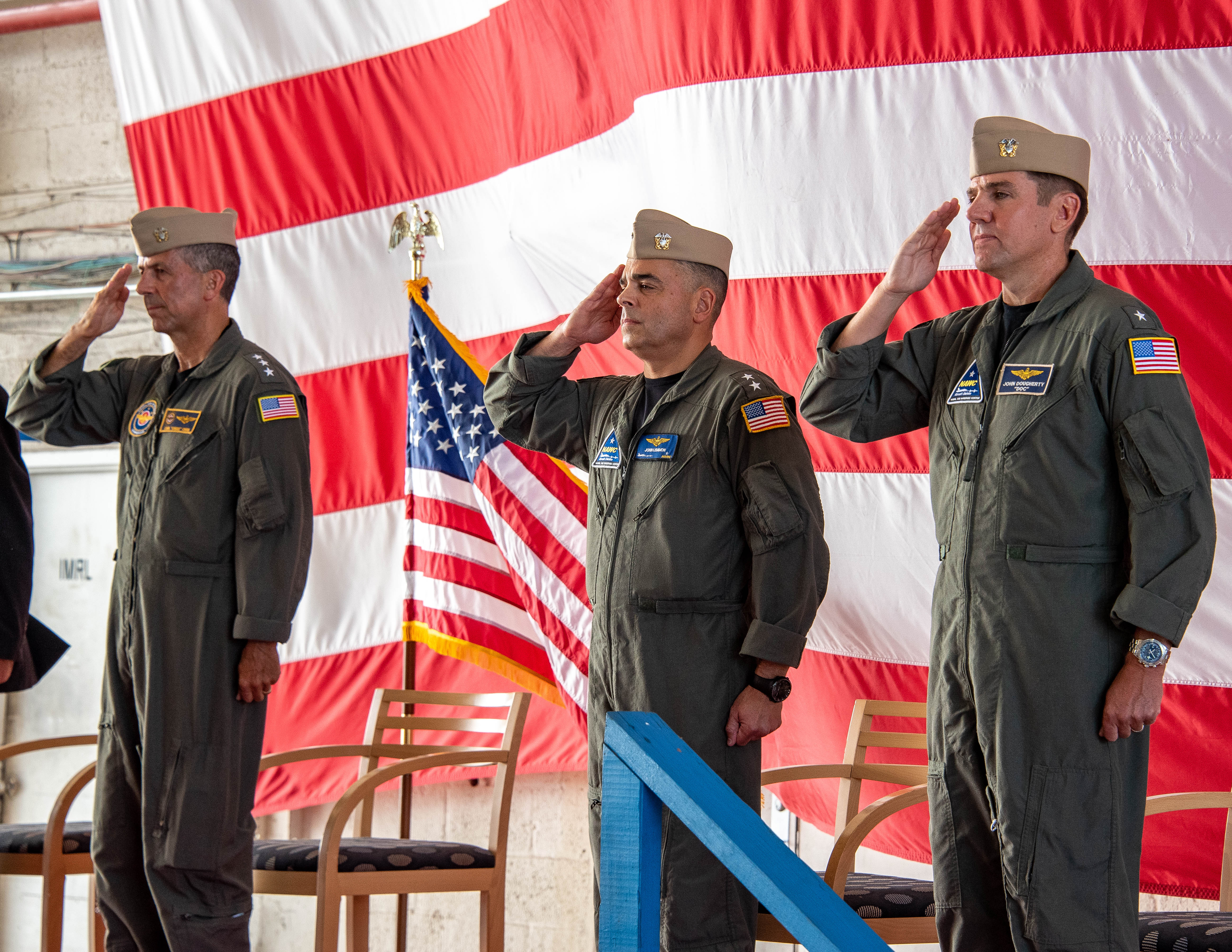 NAVAIR's Vice Adm. Carl Chebi, outgoing Rear Adm. John Lemmon, and incoming Rear Adm. John Dougherty IV salute in front of the American flag.