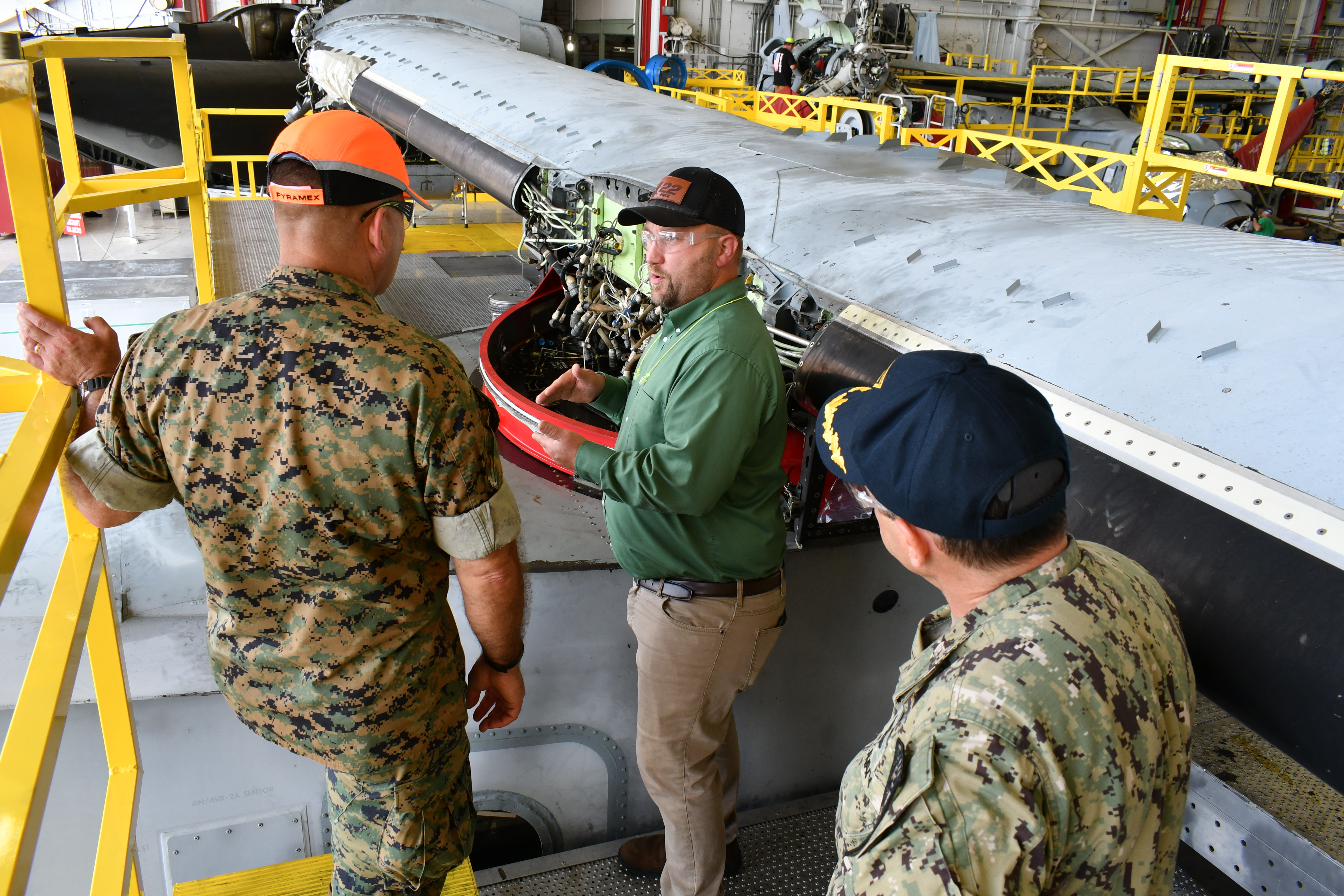 Fleet Readiness Center East (FRCE) V-22 Branch Head Andrew Rock, (center) briefs Maj. Gen. Scott F. Benedict, commanding general of 2nd Marine Aircraft Wing (MAW) and Capt. James Belmont, FRCE’s commanding officer, in front of the wing of an MV-22 Osprey.