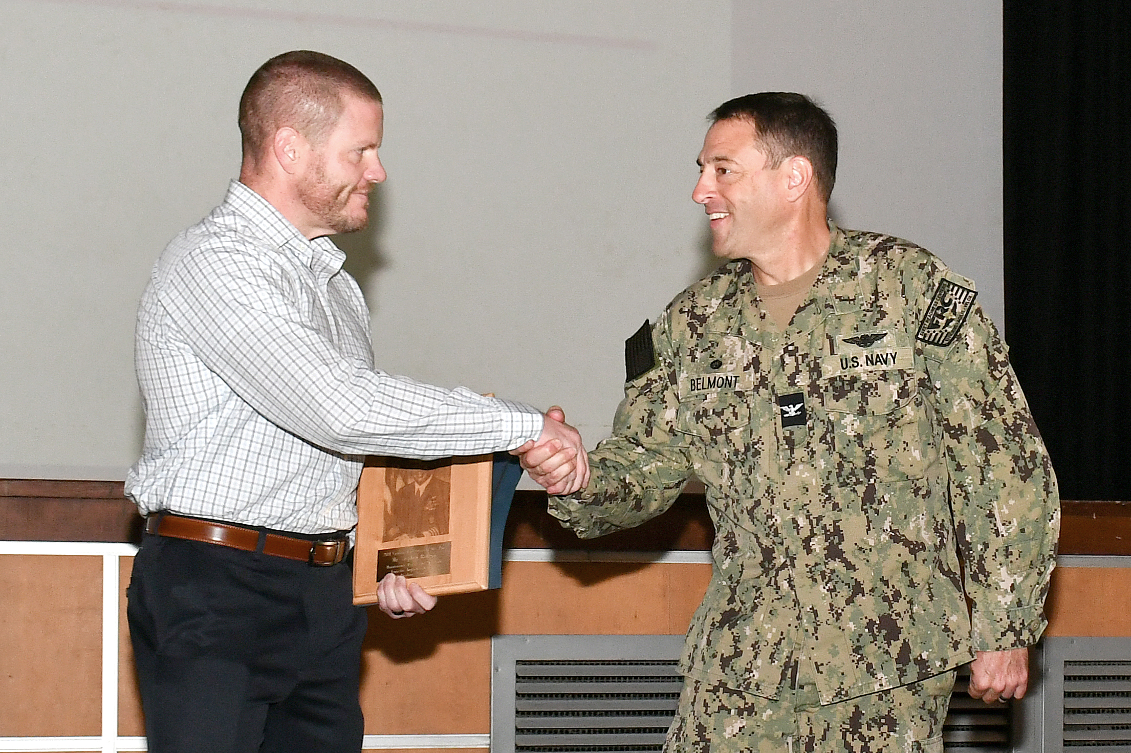 Navy captain shakes hand with civilian employee during award presentation