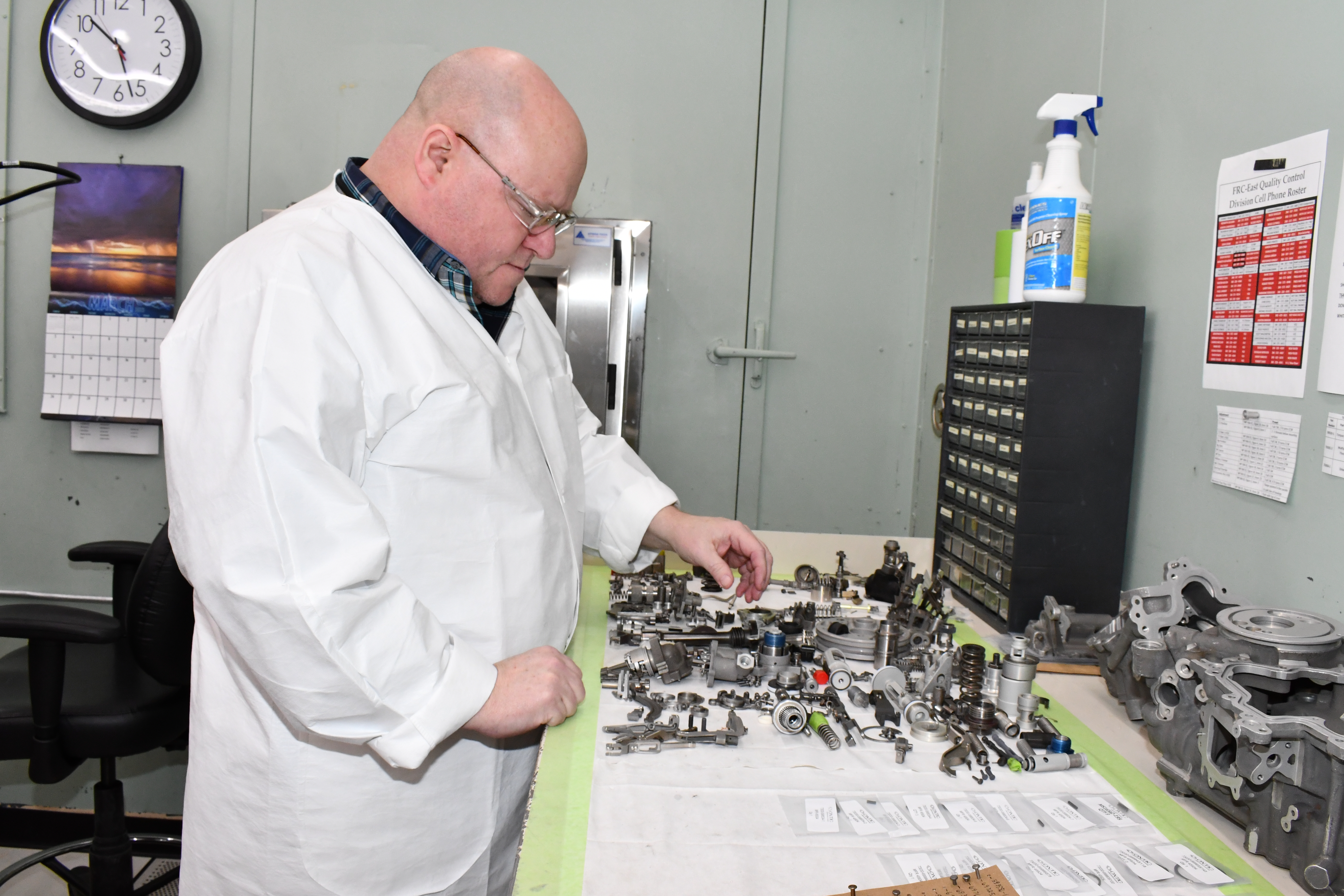 Aircraft maintainer in lab coat examines disassembled fuel control unit on clean room work bench