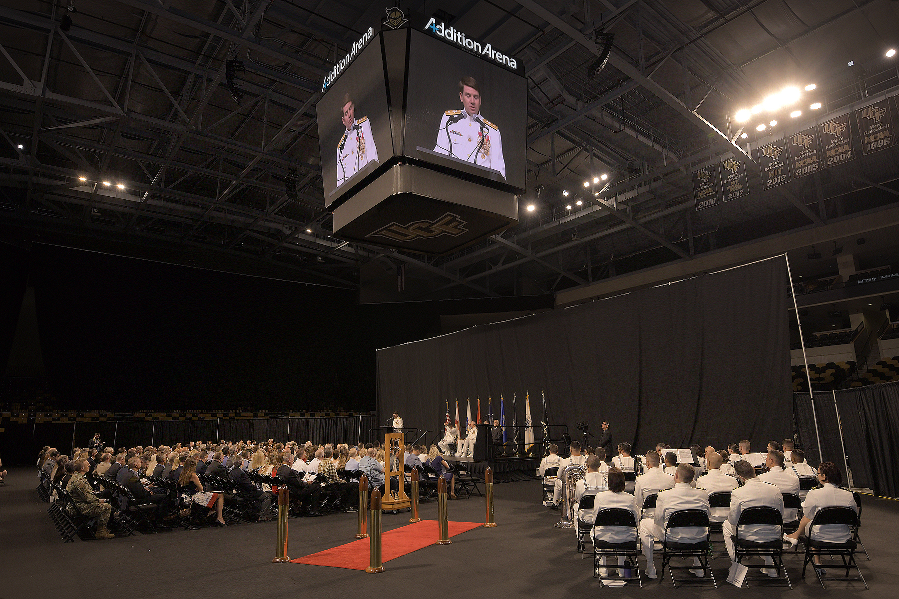 People attend a Navy change of command ceremony in an athletic arena. 