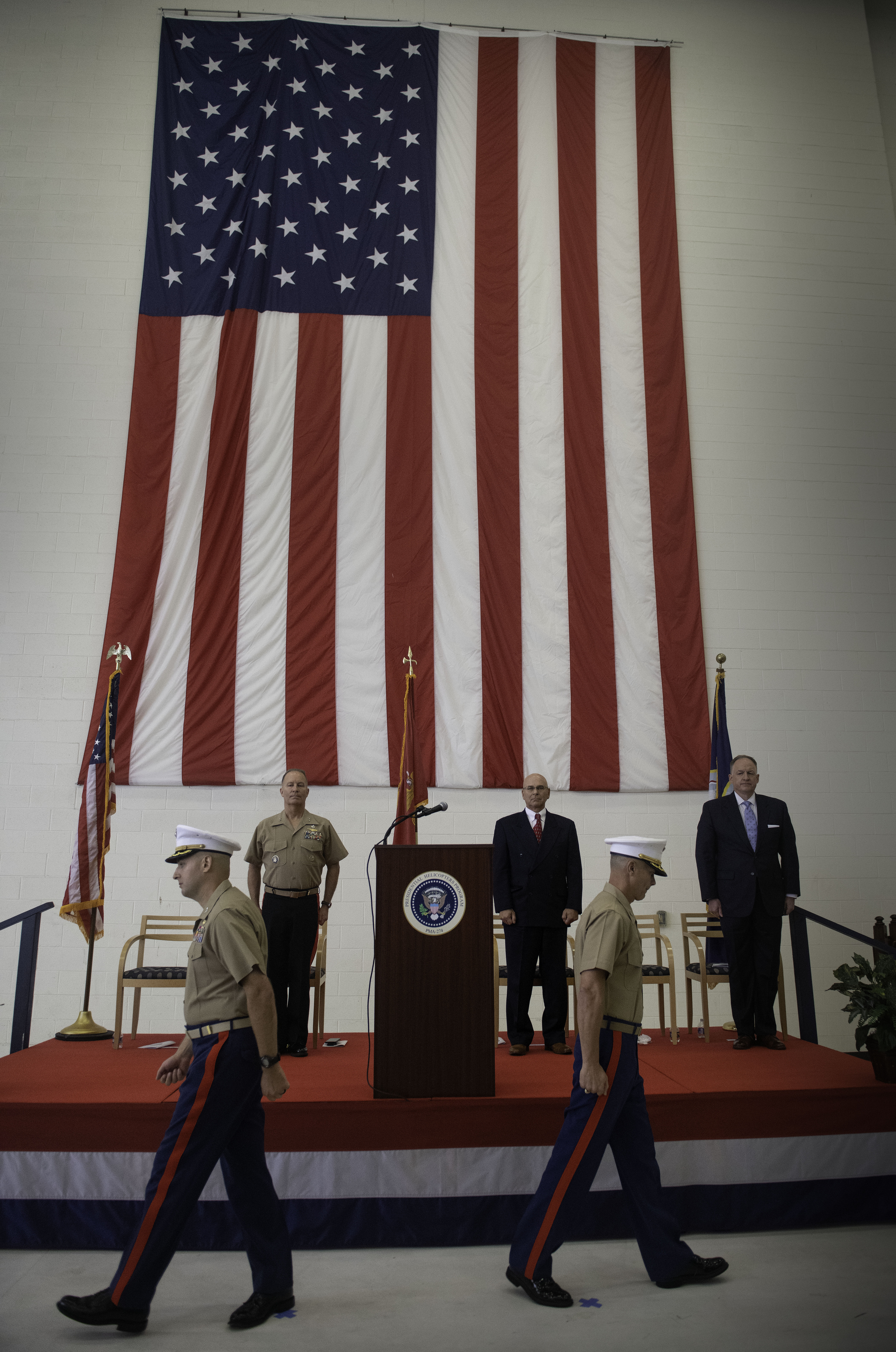 Two marines walk away from one another with a large flag in the background after officially changing command