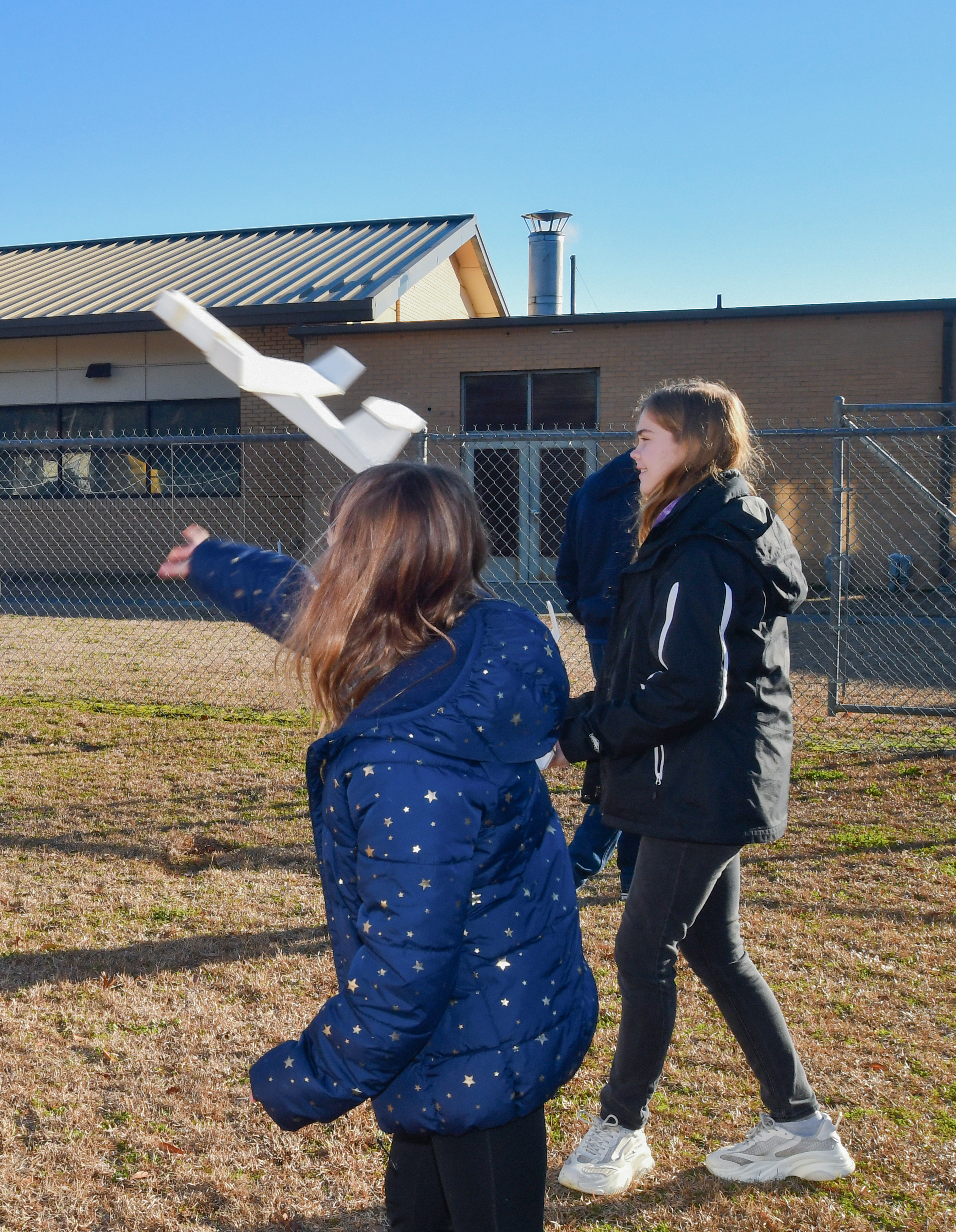 Two female students stand outside and one is throwing a foam airplane into the air