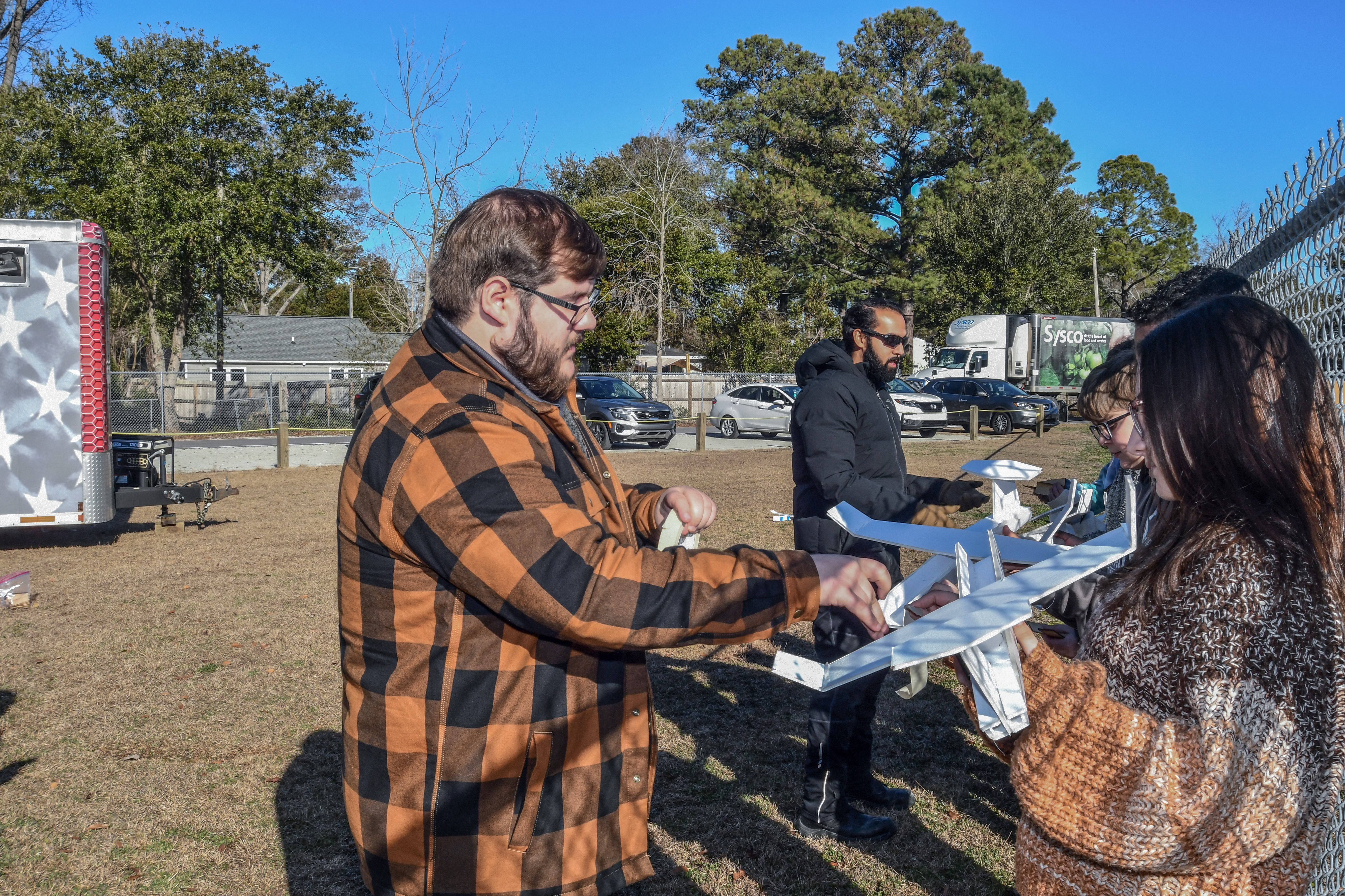 Man stands on the left helping female student on the right with foam airplane