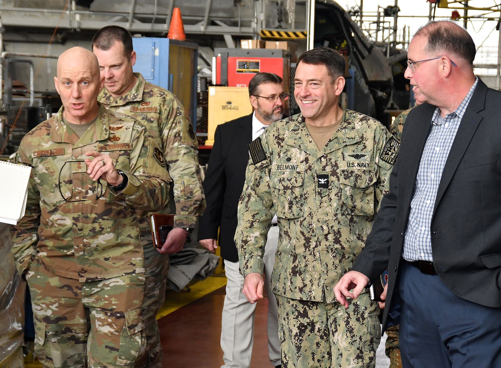 Group of military officials walks down aisle in aircraft hangar