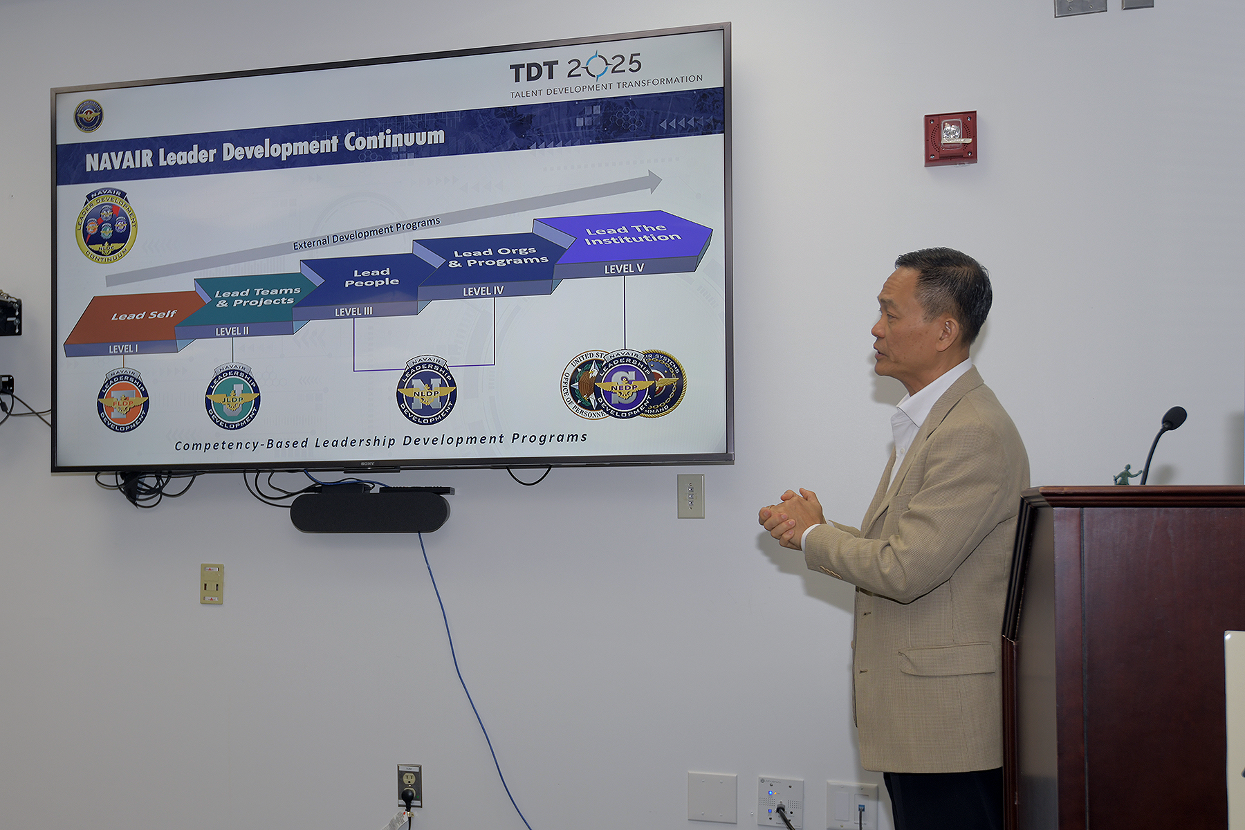 Man standing in front of a large screen monitor using PowerPoint slides while speaking. 