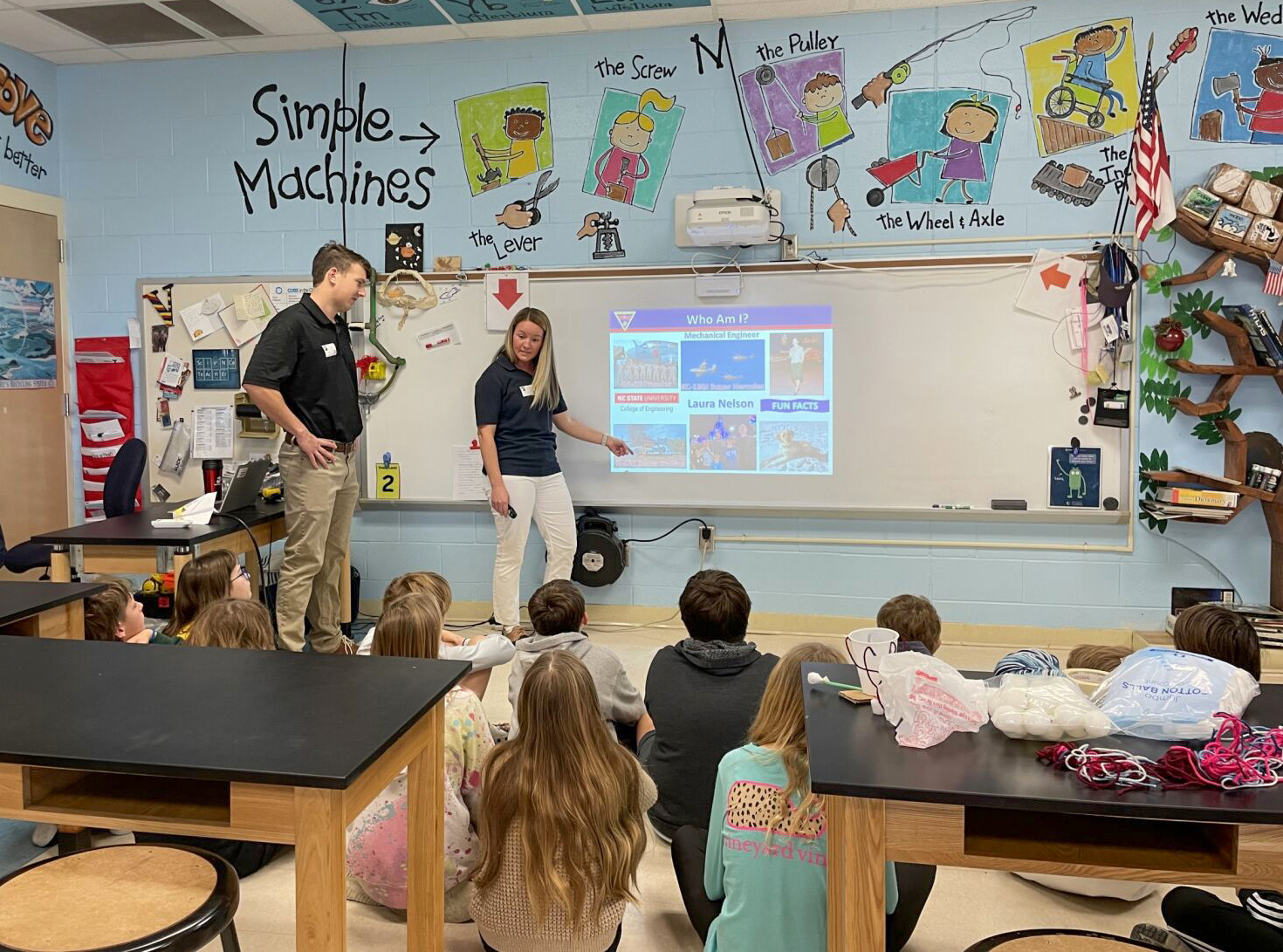 Two adults show presentation to students sitting on floor in classroom 