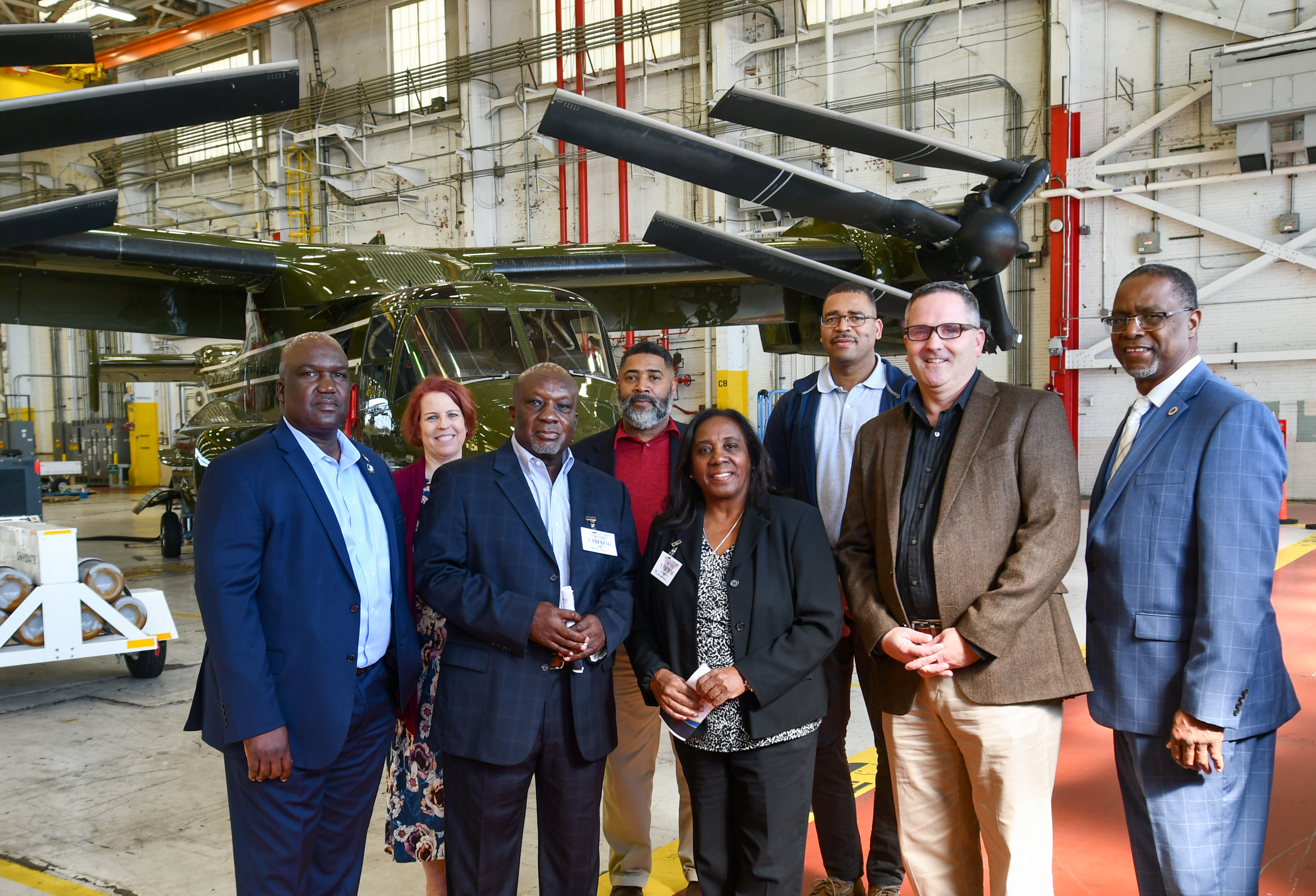 Eight individuals stand in front of a green V-22 aircraft