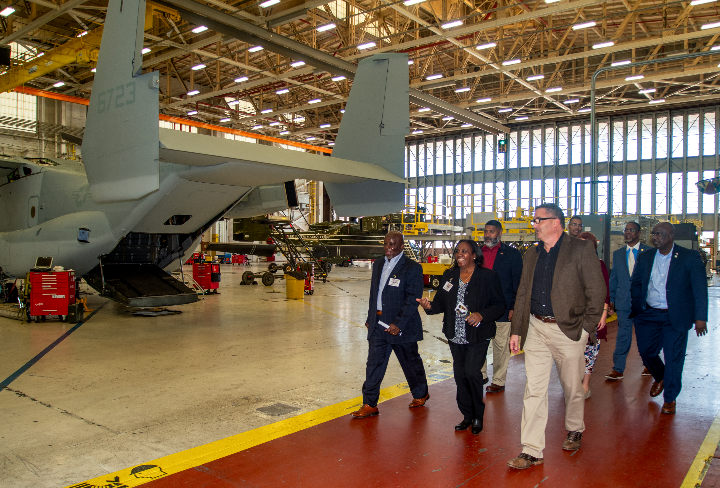 eight individuals walk on a red pathway next to the rear of an aircraft 