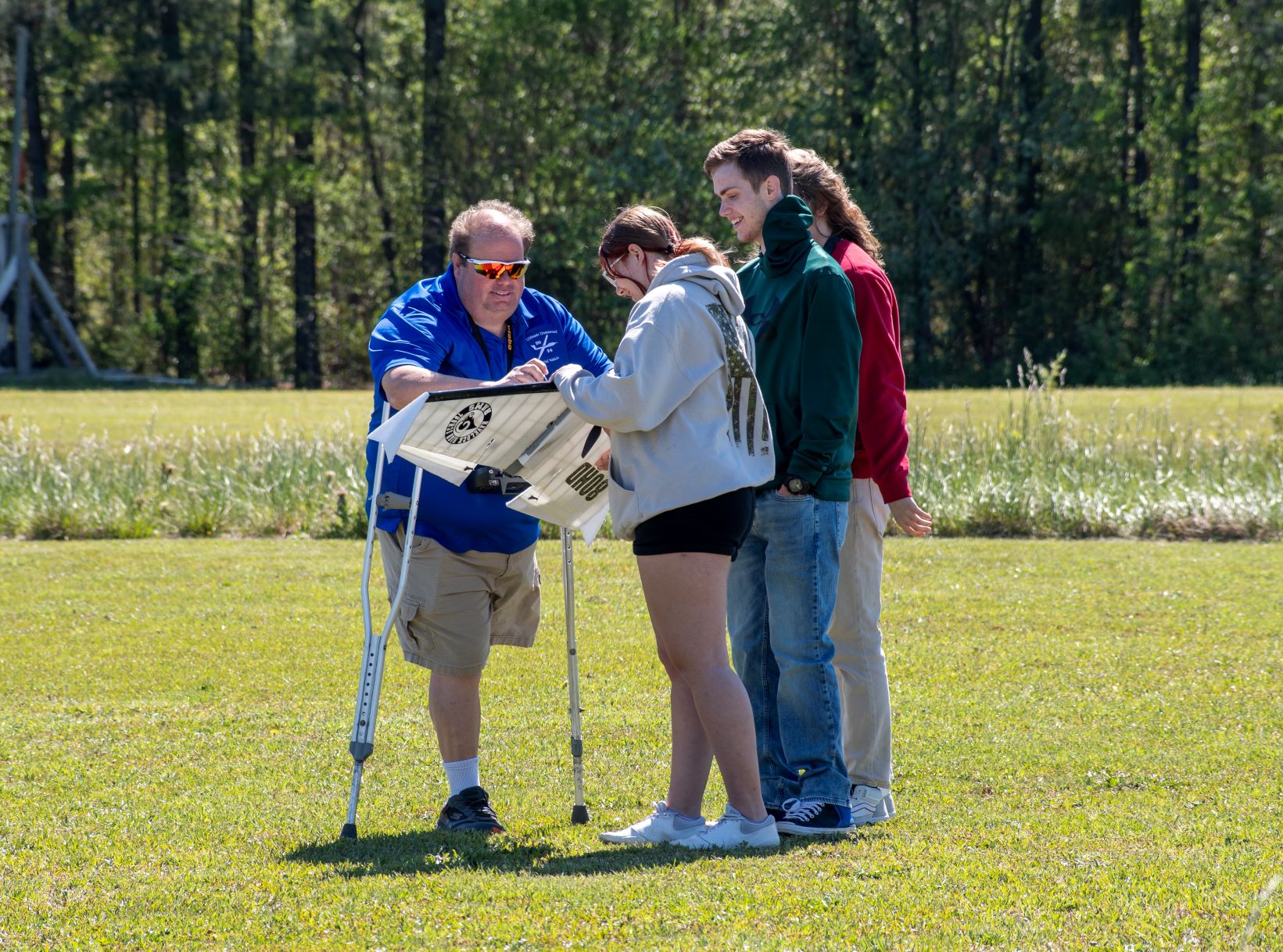 Three students stand with a gentleman on crutches outside 