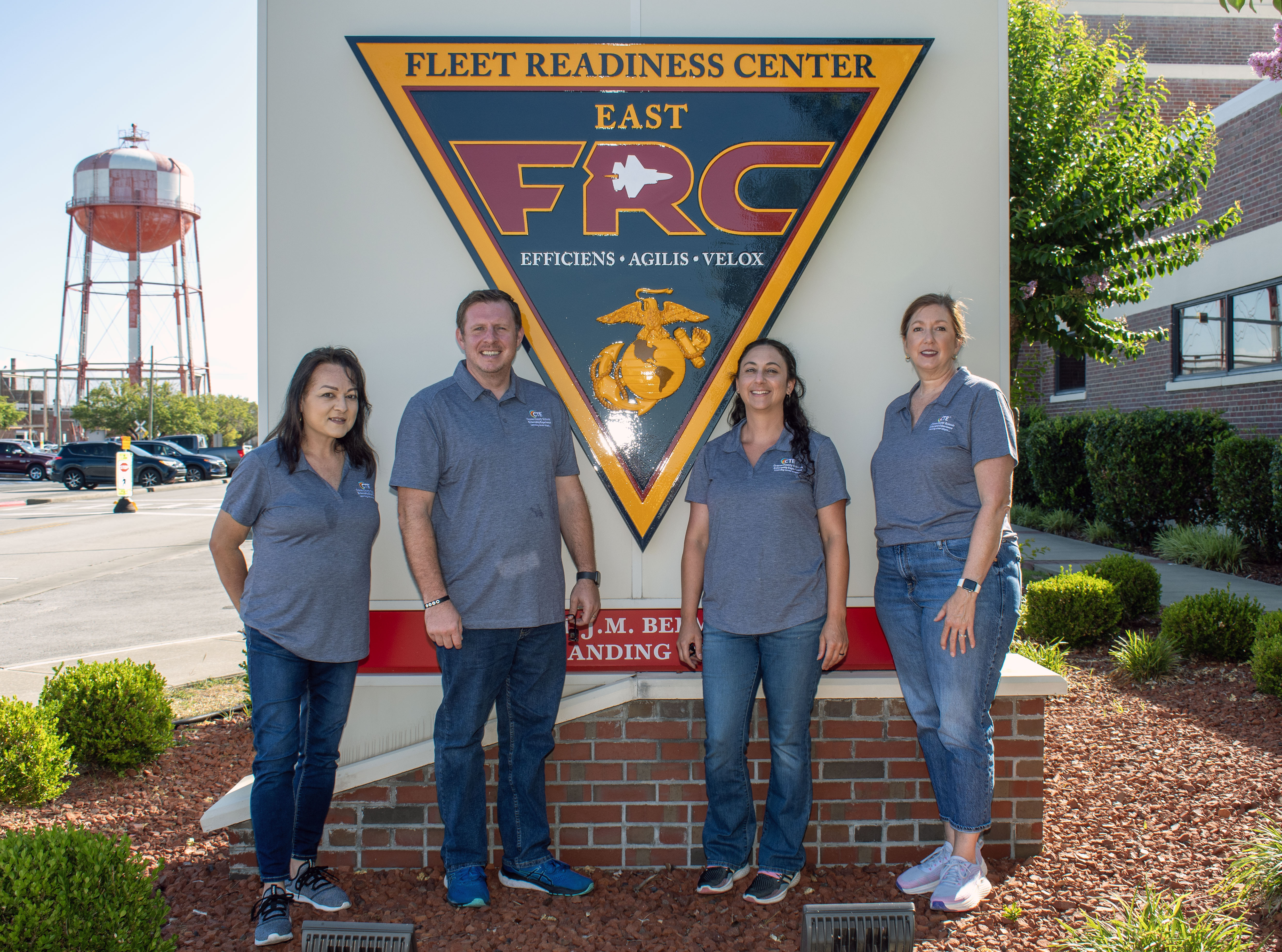 Four adults standing outside in front of FRCE sign