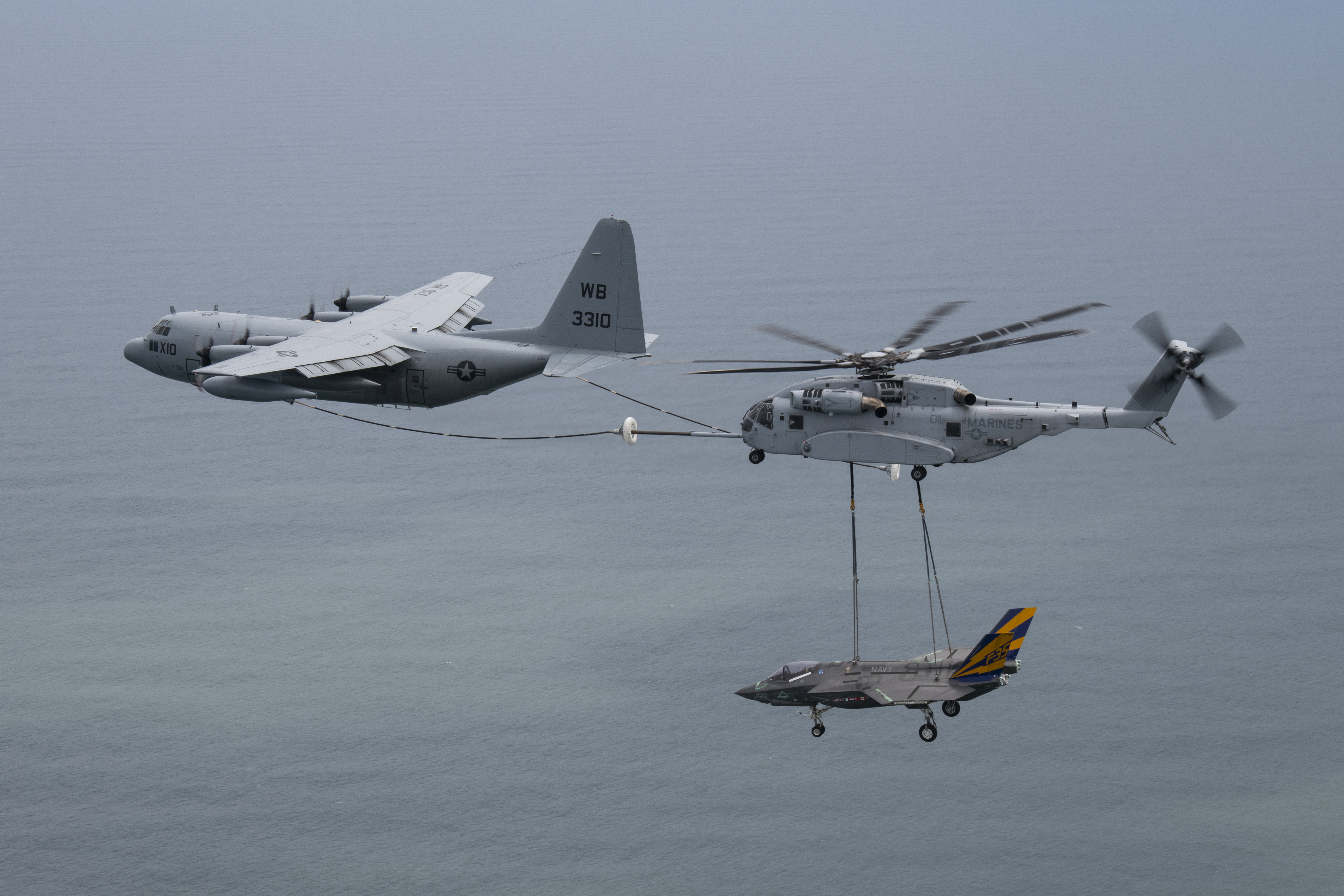 C-130 plane aerial refuels a CH-53K helicopter while carrying an F-35 airframe in the sky