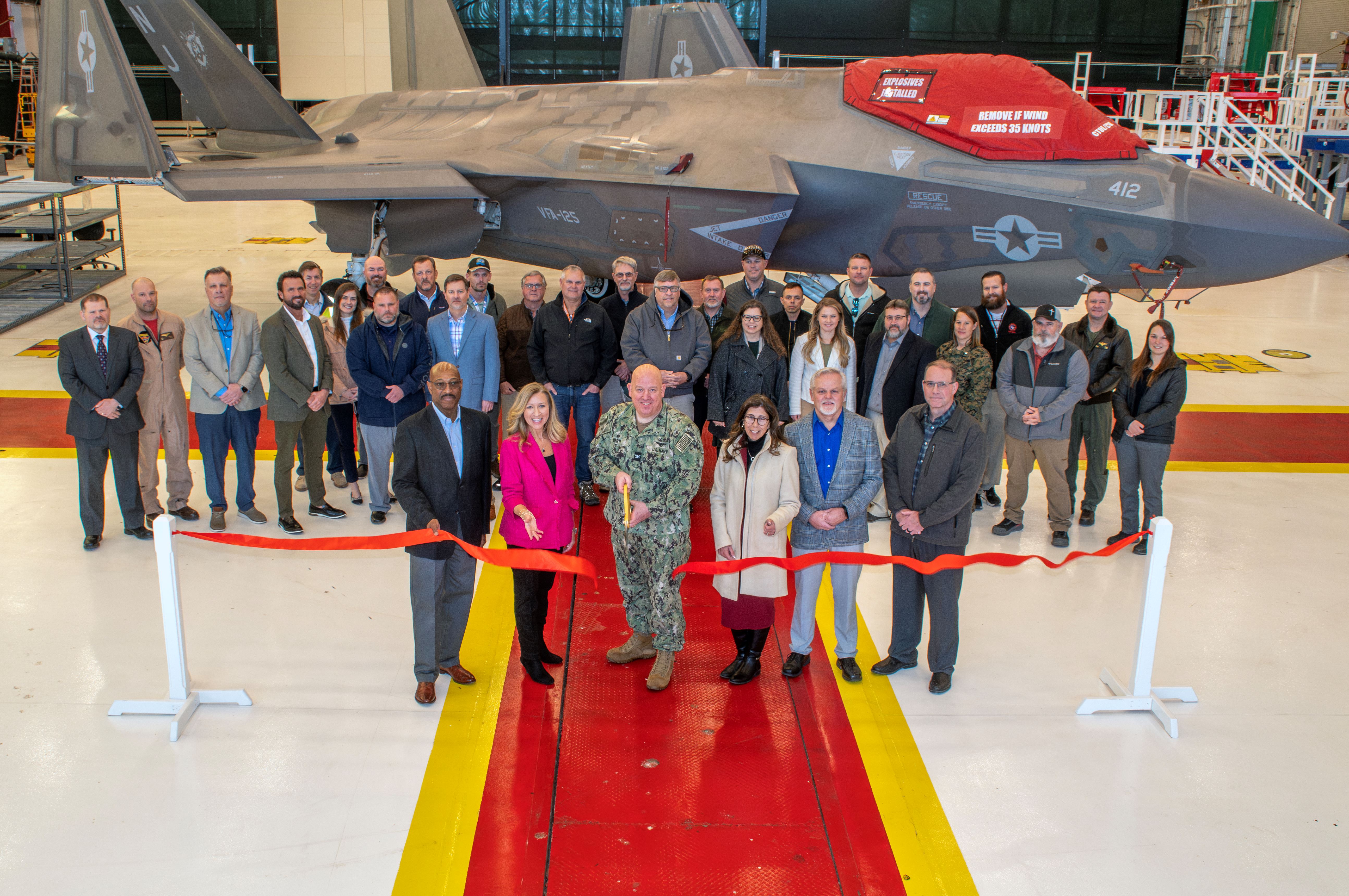 Group of people posing in front of F-35 aircraft during ribbon cutting 
