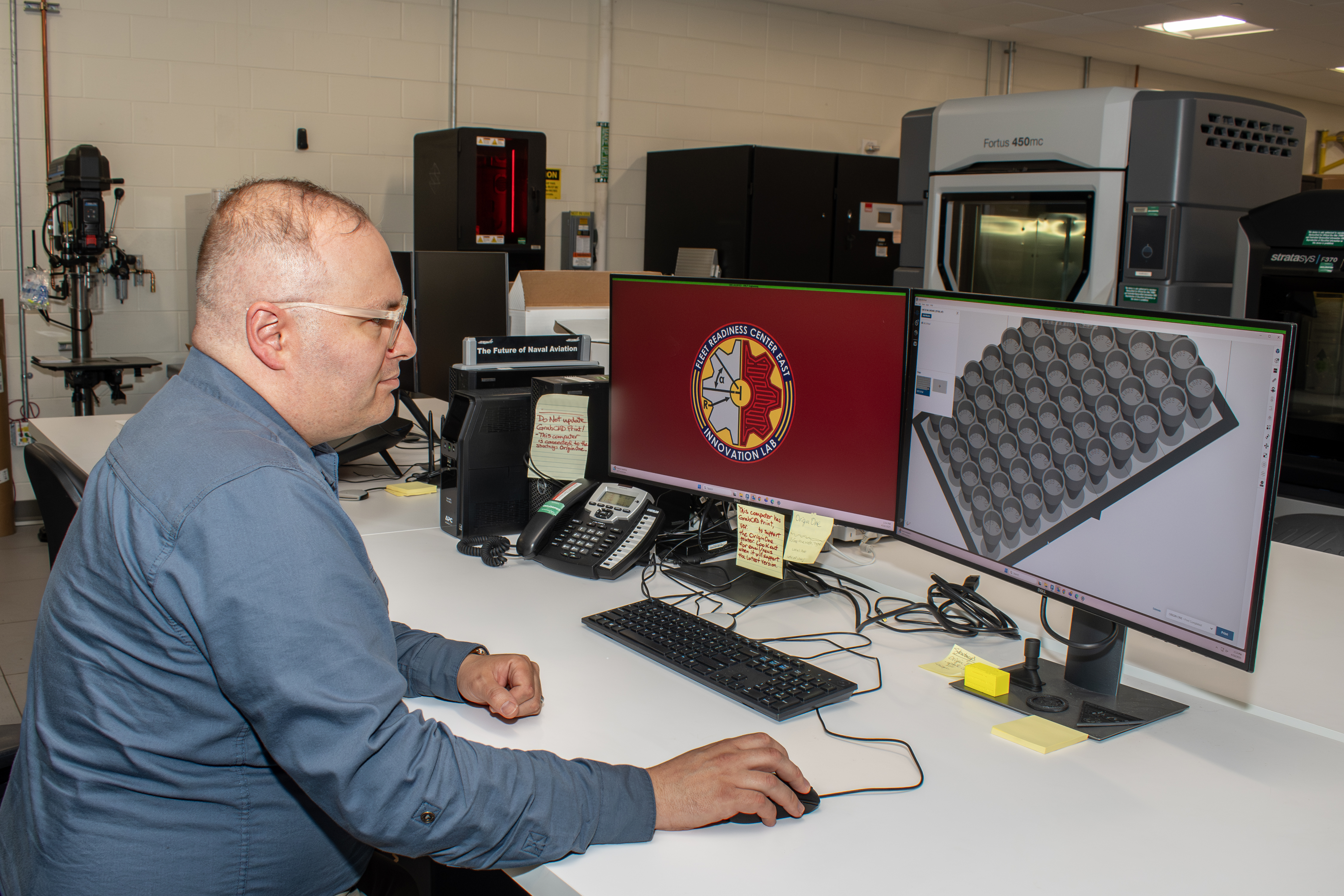 Engineer sitting at desk uses computer mouse to work with 3D printing model displayed on computer monitor