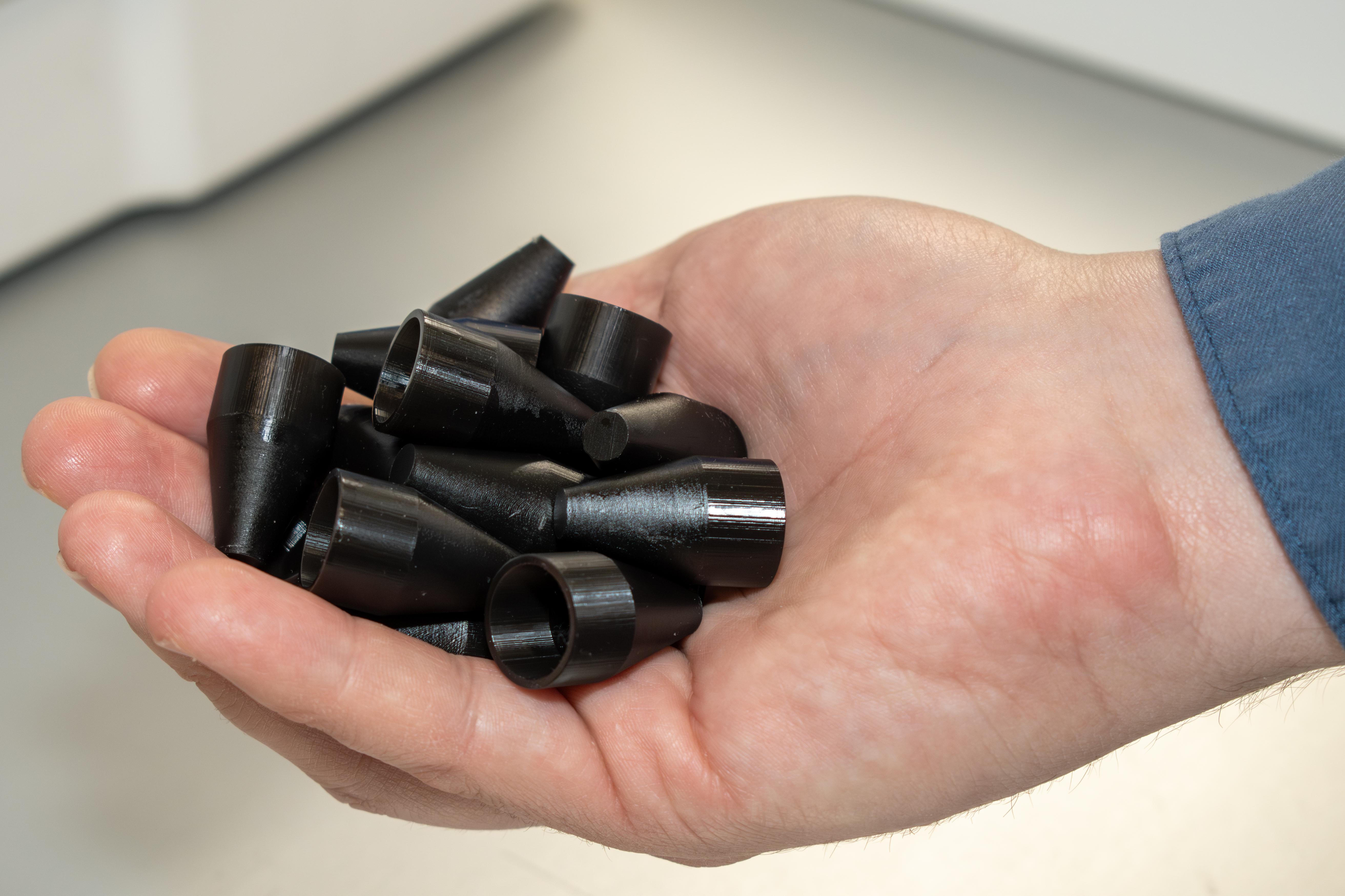Close-up image of a man's hand holding several small, black polymer cones 3D printed as a maintenance aid for F-35 Lightning II aircraft
