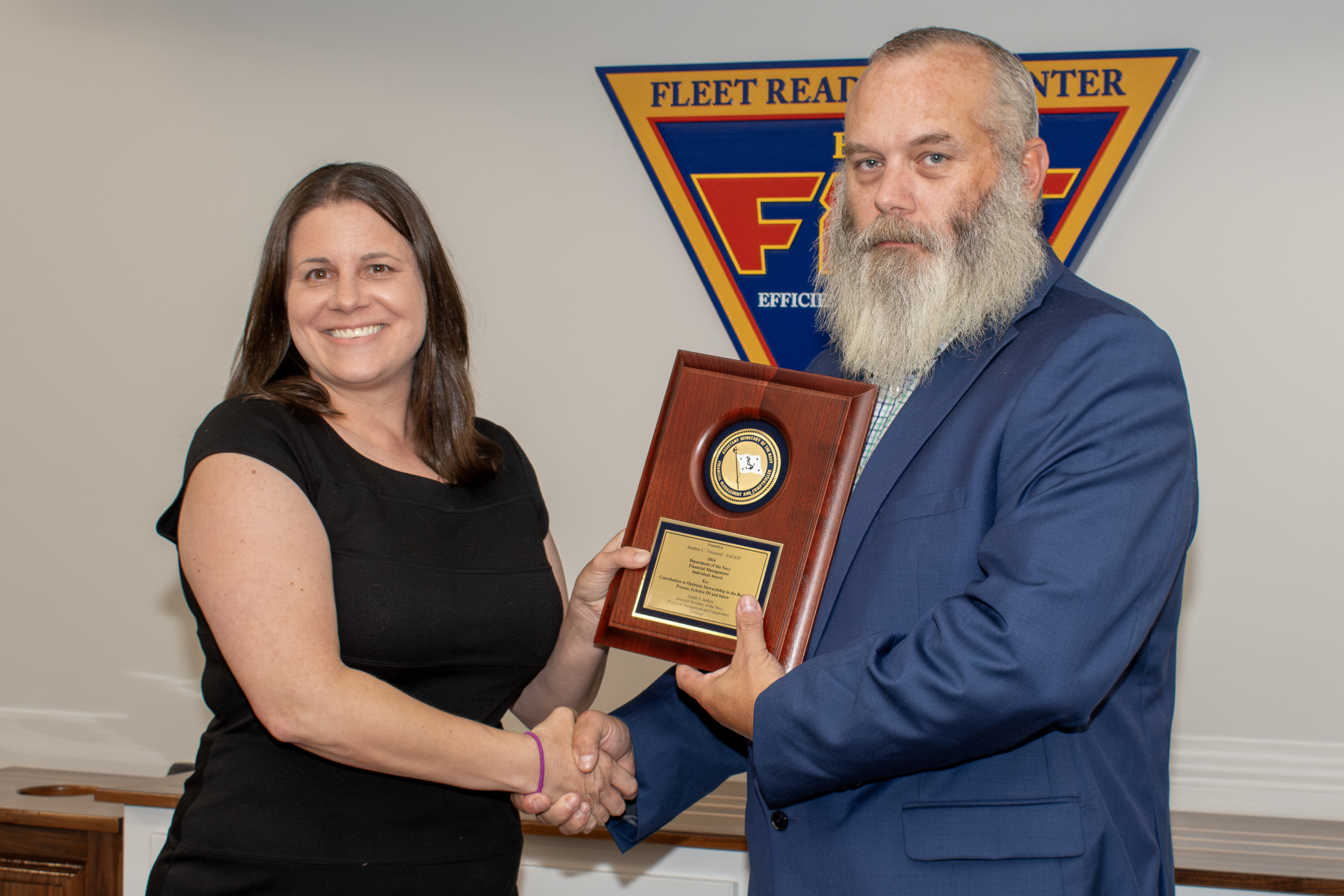 Man and woman shaking hands while holding award plaque