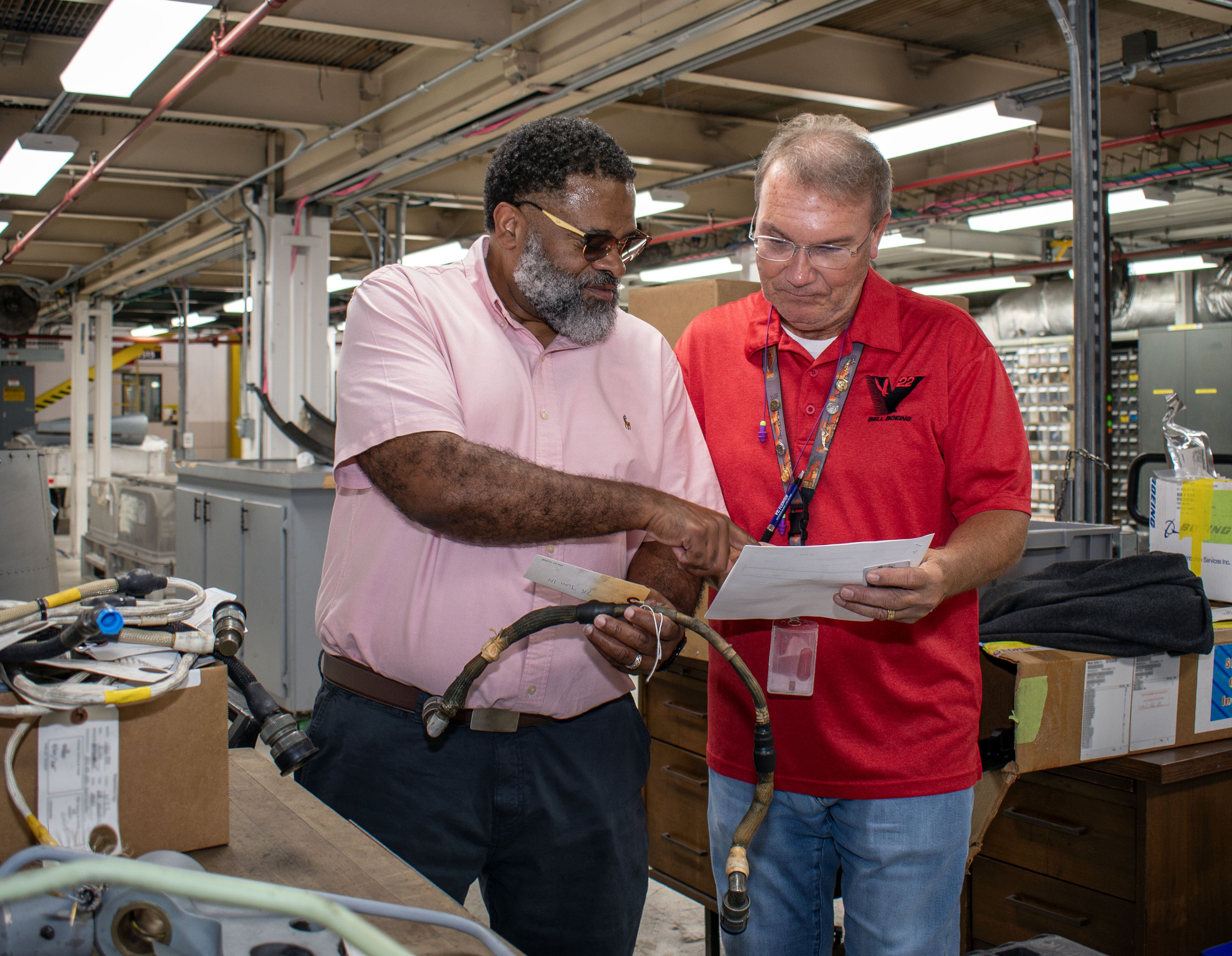 Man in pink shirt shows man in red shirt something on paper 