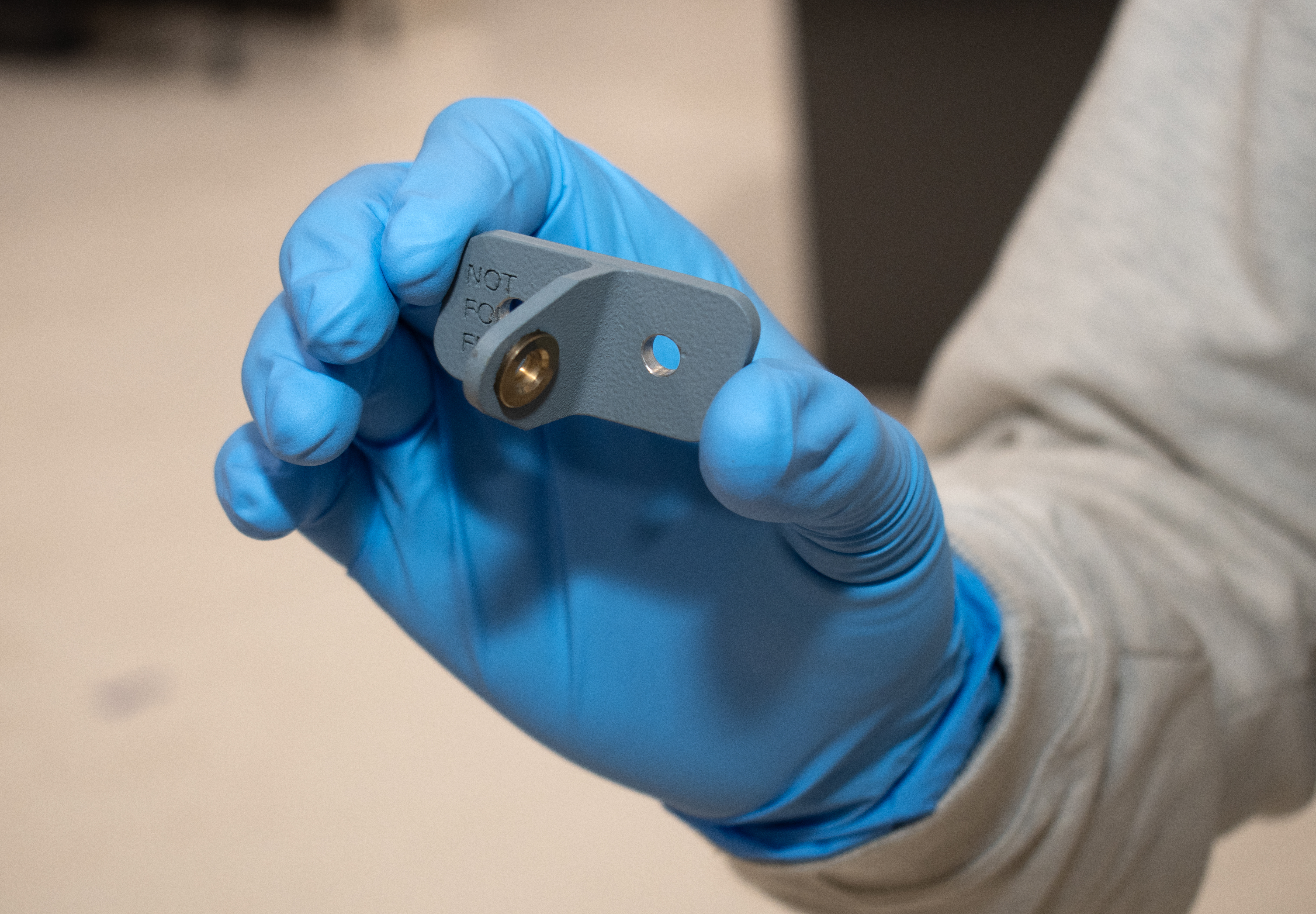 Person wearing blue gloves holds small grey metal part