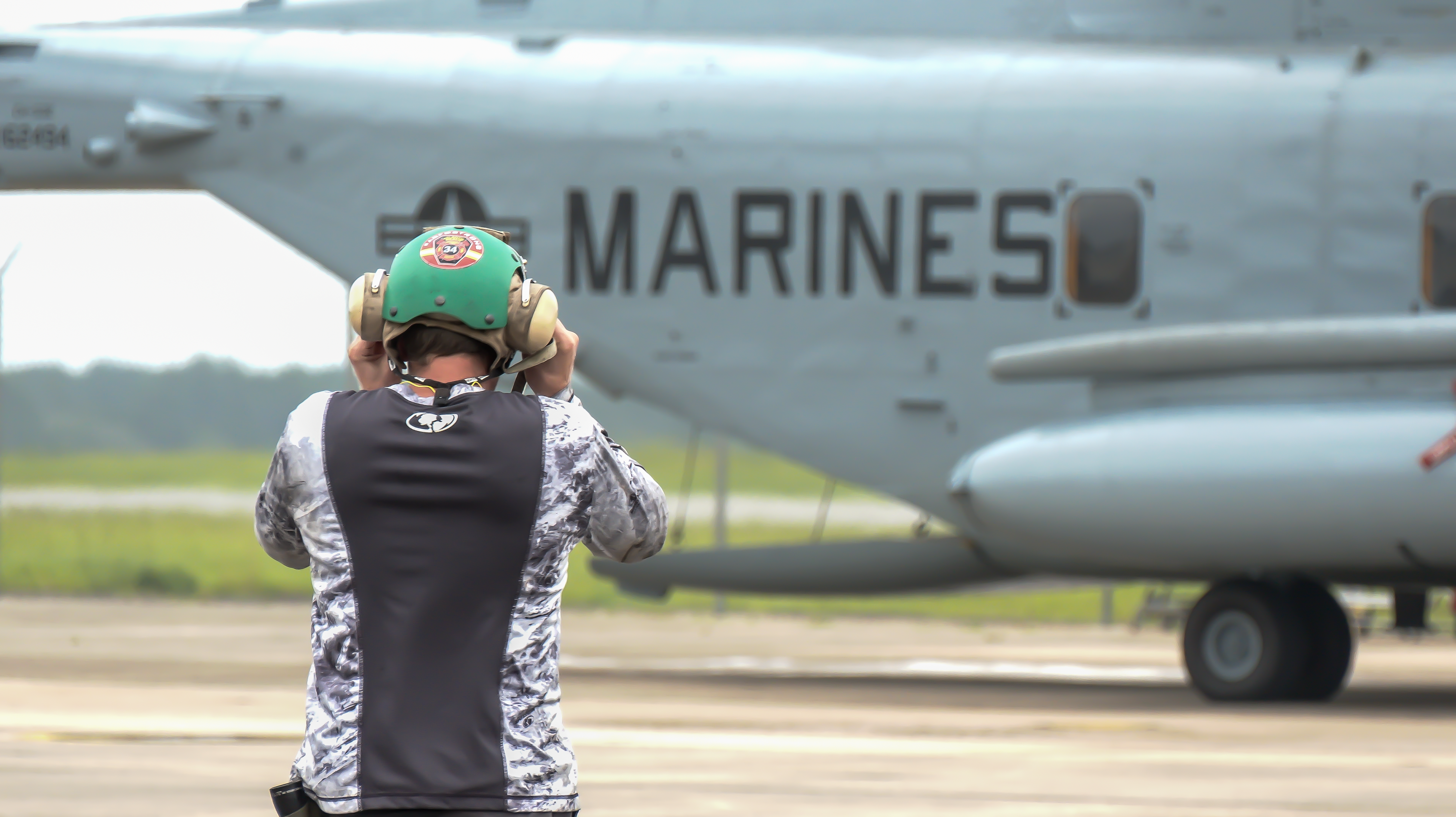 Man in black and grey shirt looking at "Marines" on military aircraft