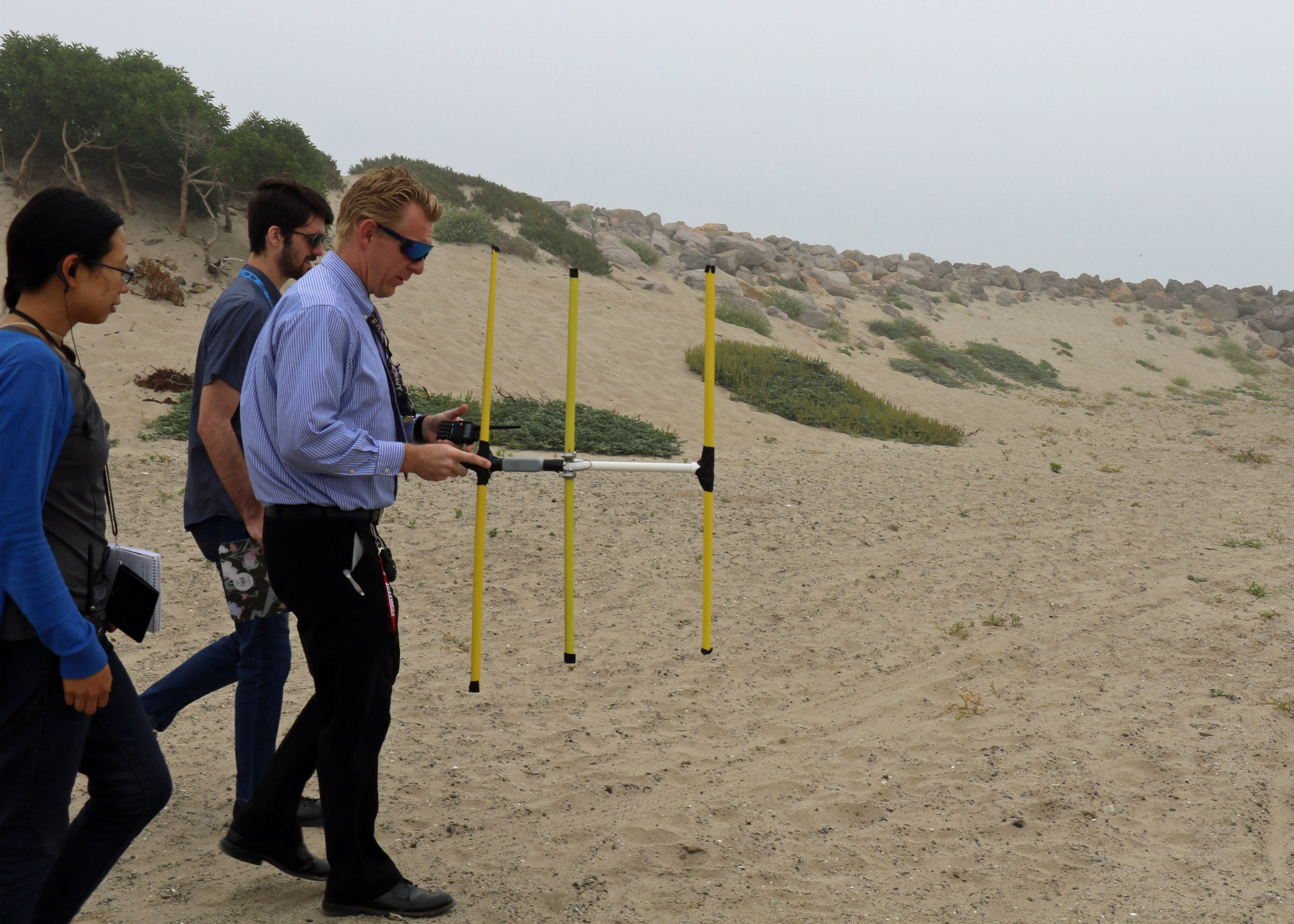 Diane Phung, Thomas Hentges, and Phillip Porter hunt for a transmitter hidden on the beach in Point Mugu, California, 