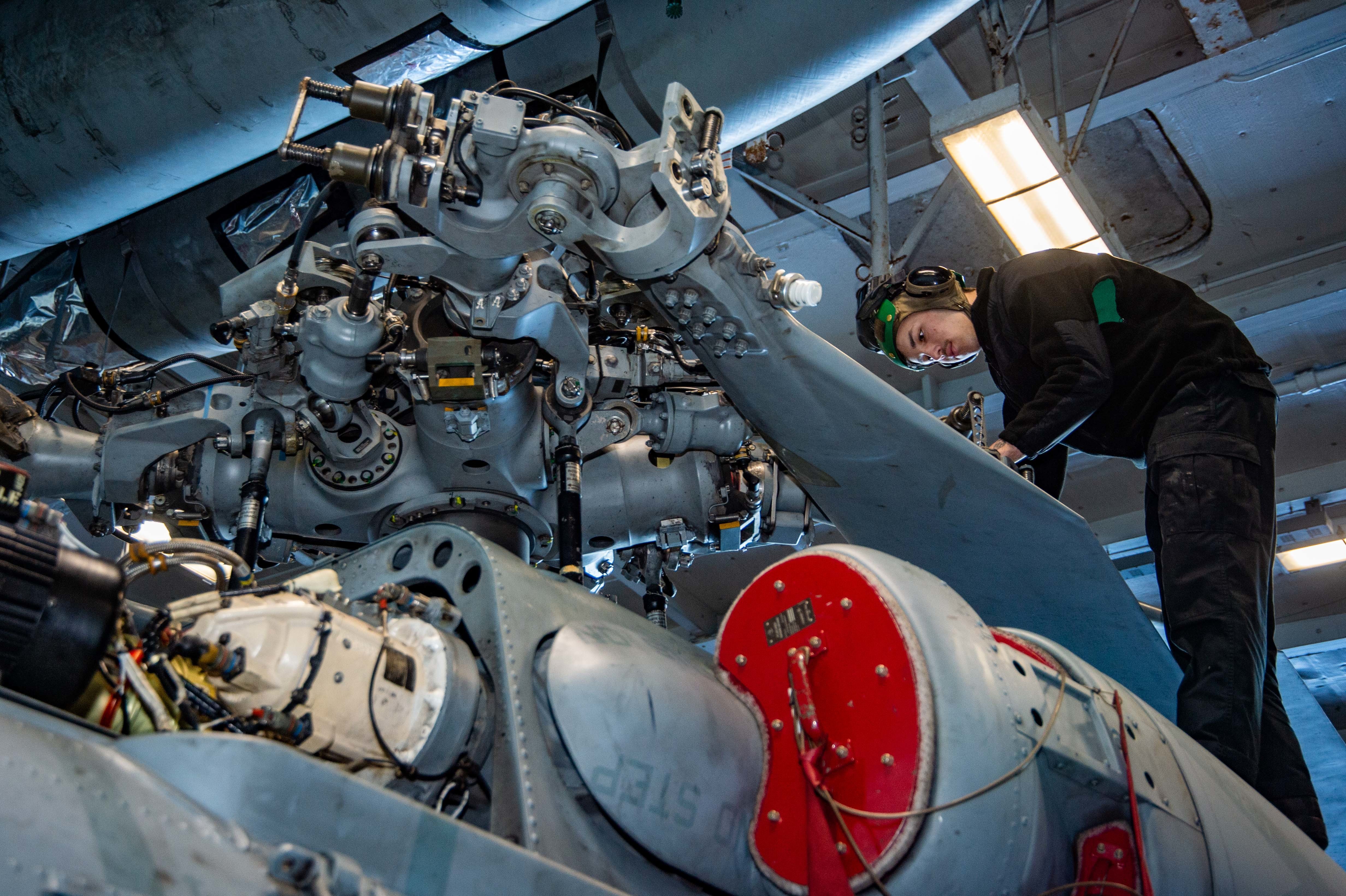 A Sailor inspects rotor gear for corrosion aboard the MH-60S Seahawk Helicopter.