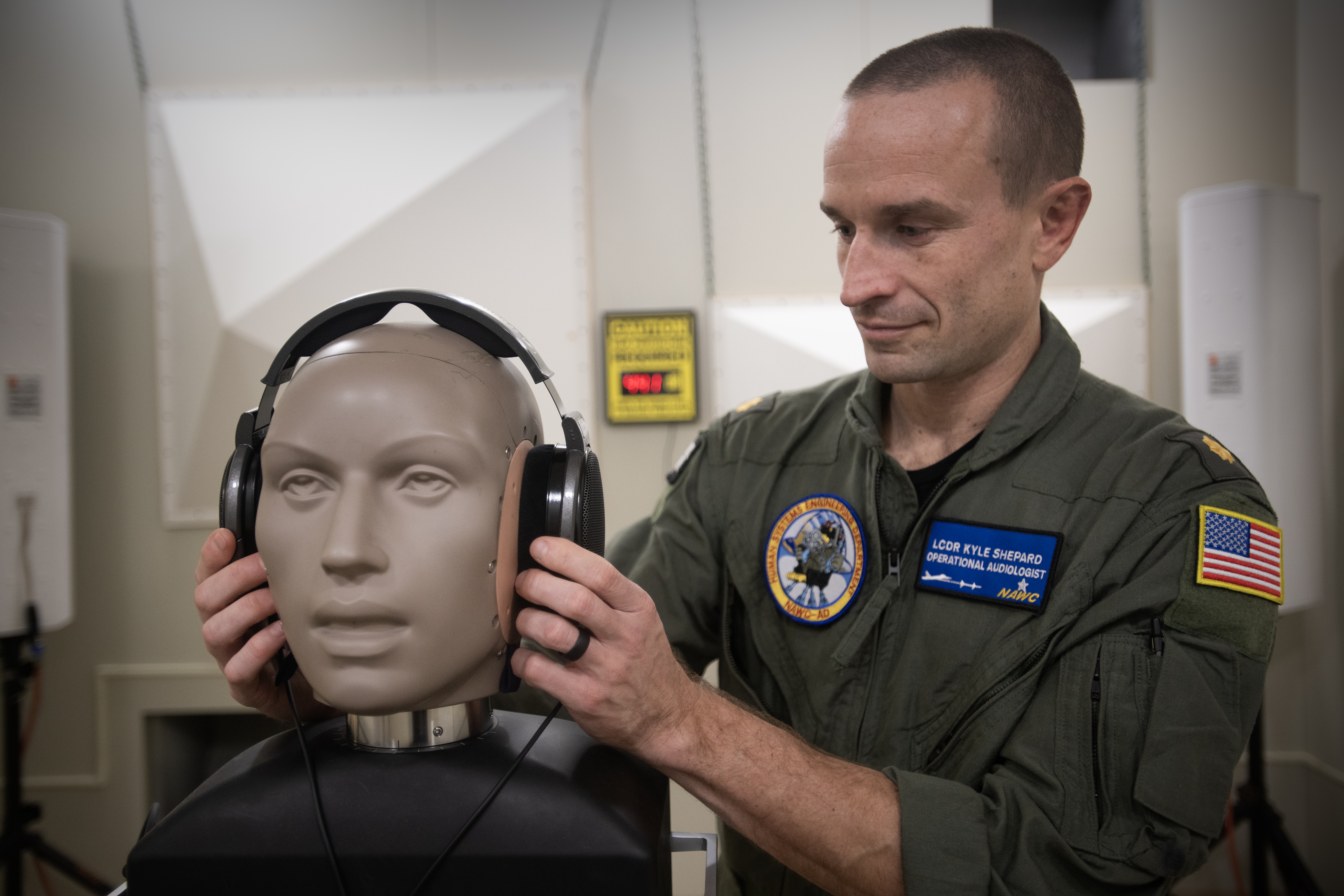 An aeromedical officer fits a dummy with headphones for audio testing in a lab.