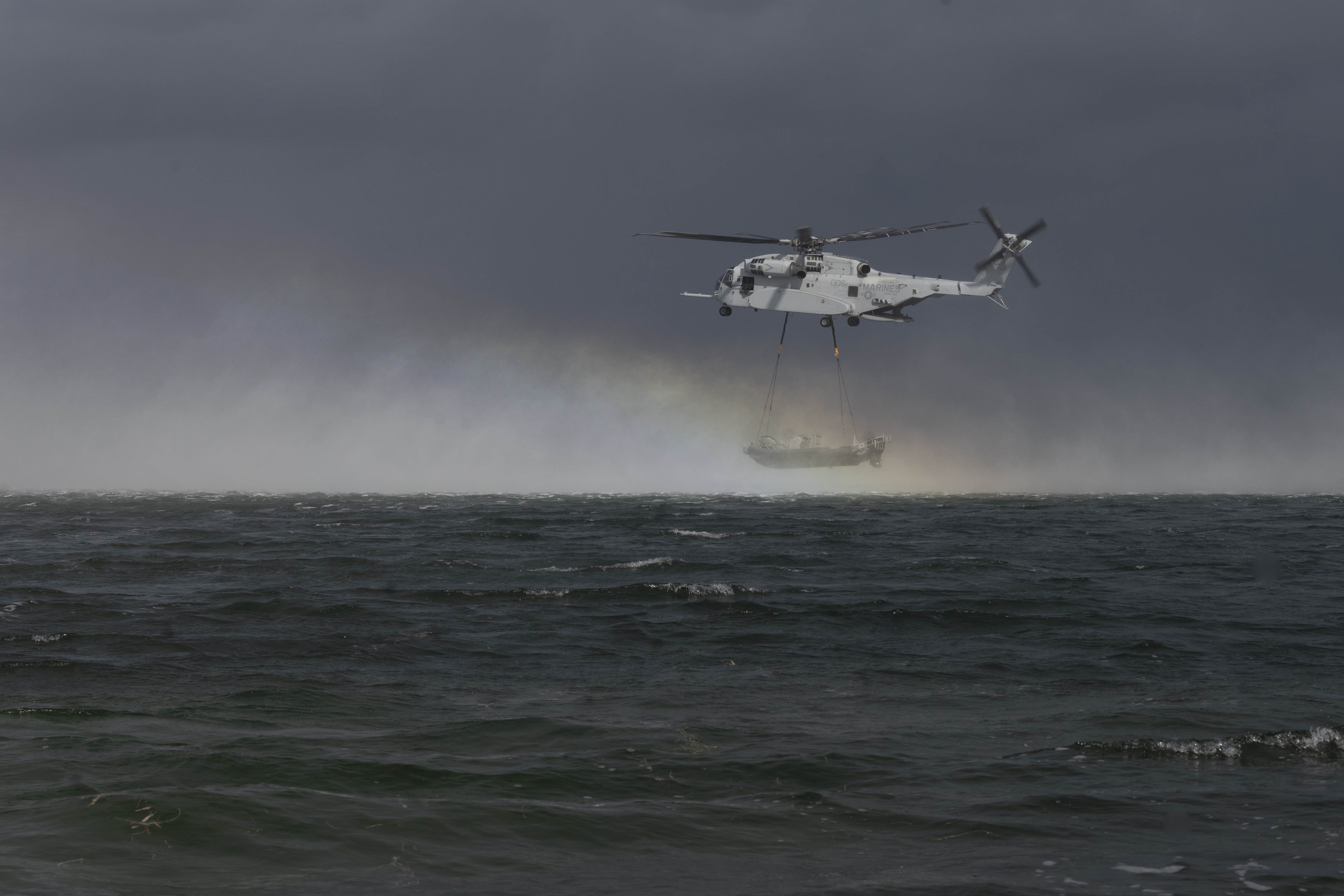 Helicopter hovering over open ocean carrying an inflatable boat