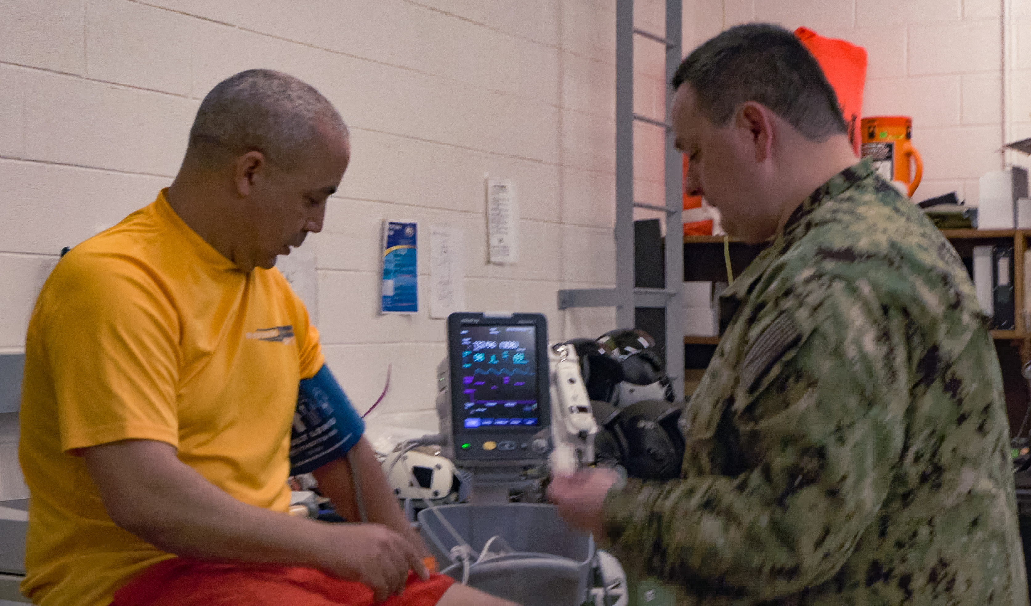 A uniformed Navy audiologist takes vital sign readings for another sailor.