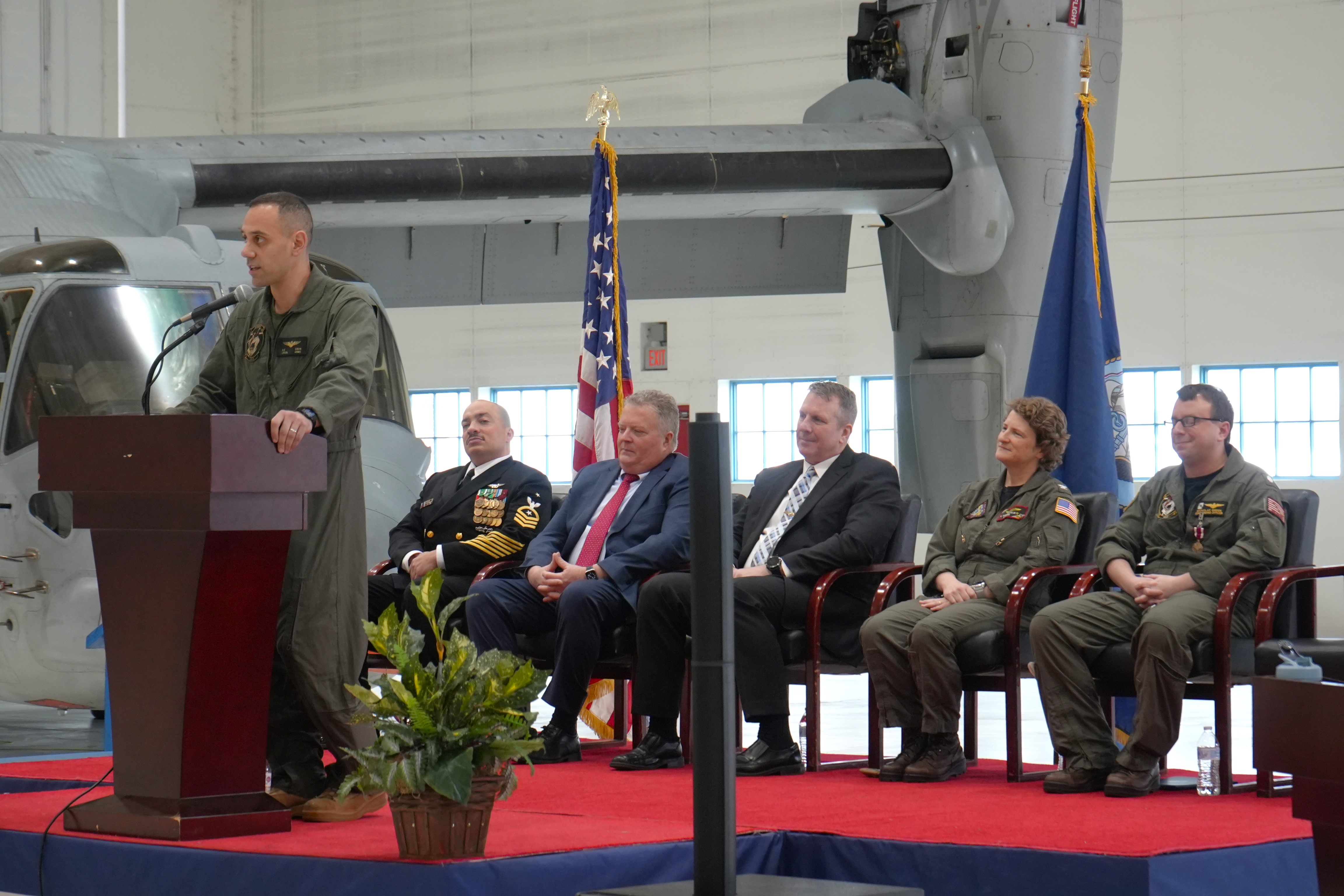 The HX-21 commander speaks at a podium during a change of command ceremony.