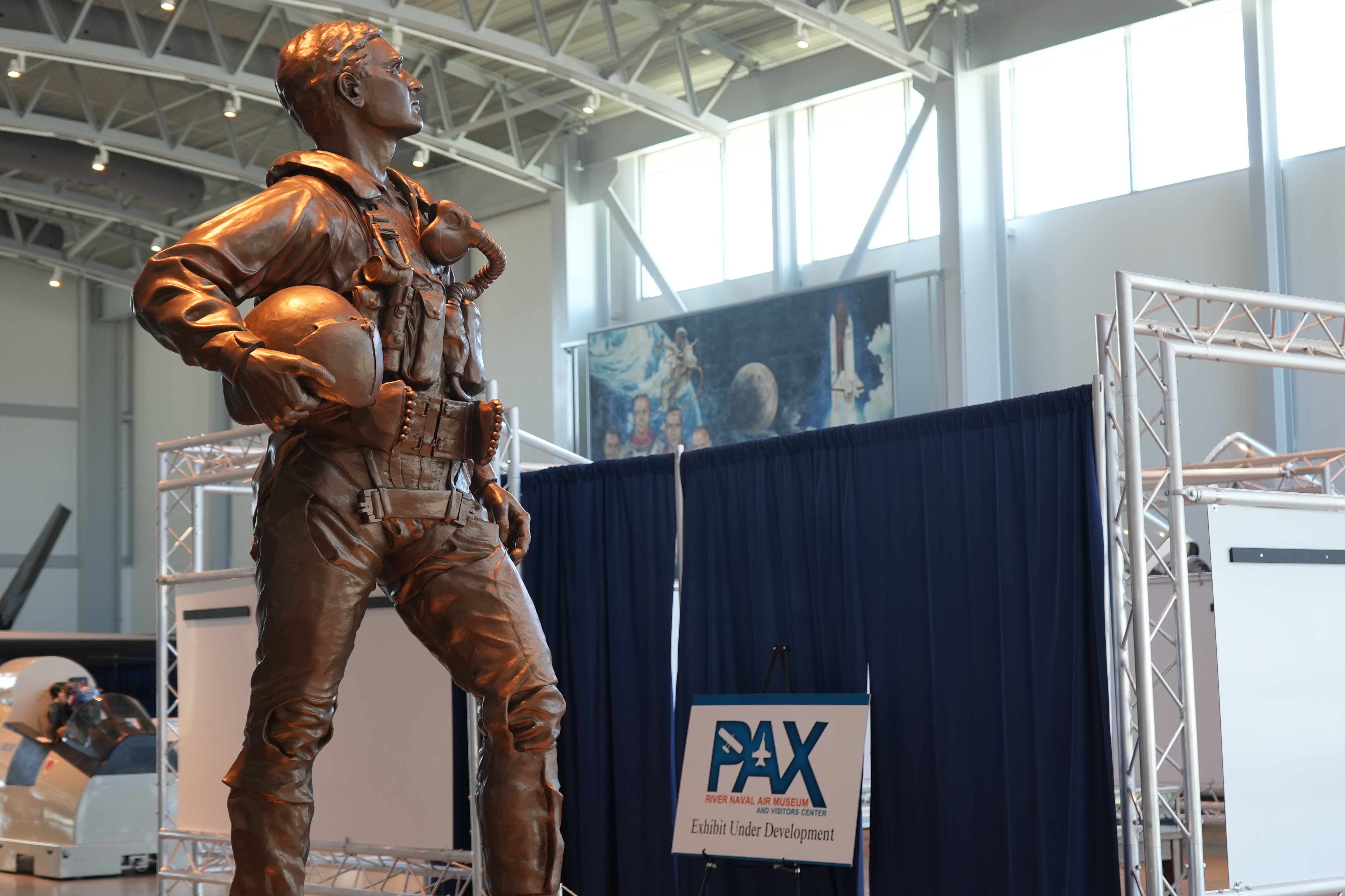 A bronze statue of a test pilot stands in front of a curtained museum exhibit under construction.
