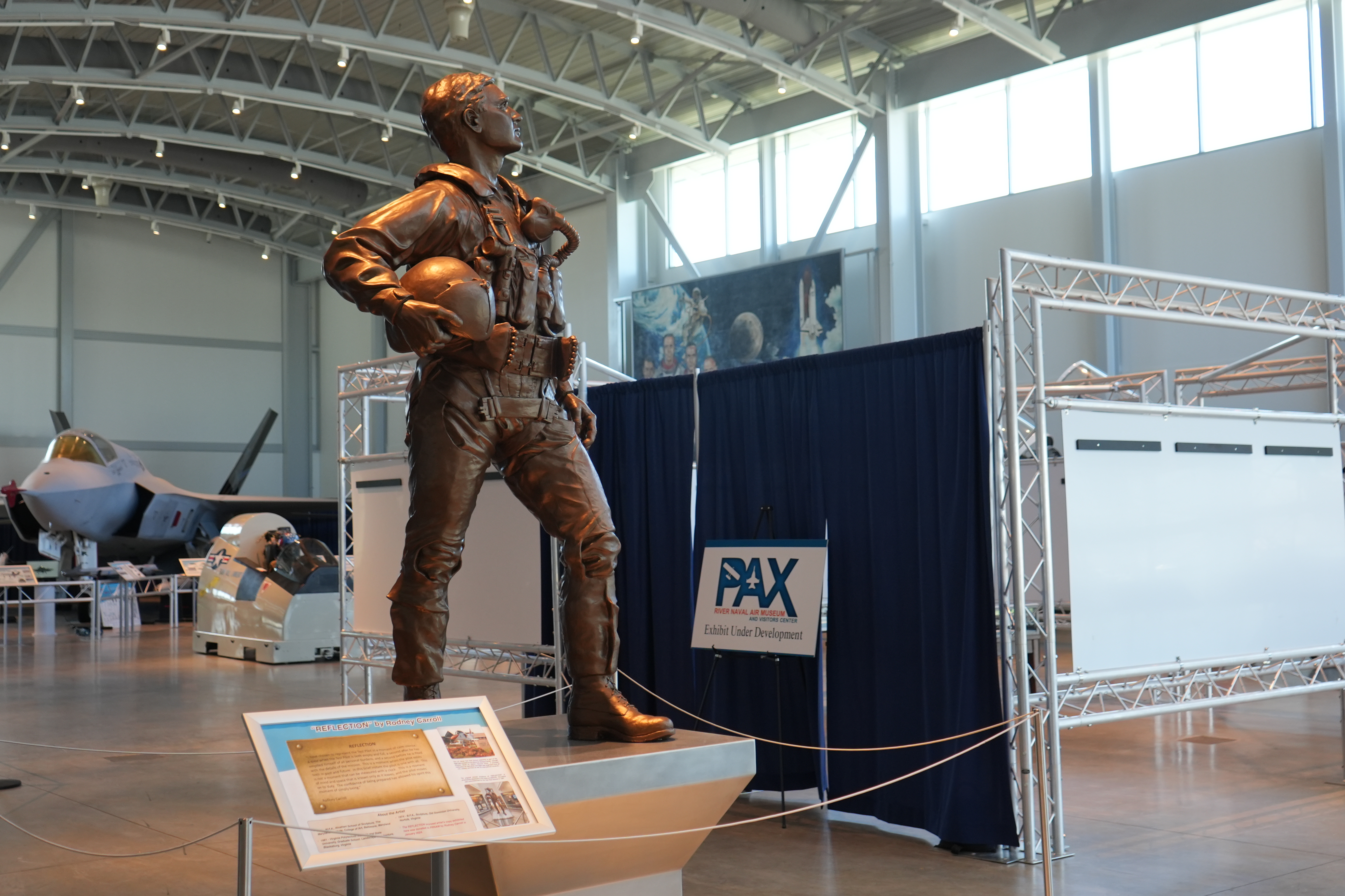 A bronze statue of a test pilot stands before a museum exhibit curtained off from visitors while under construction.