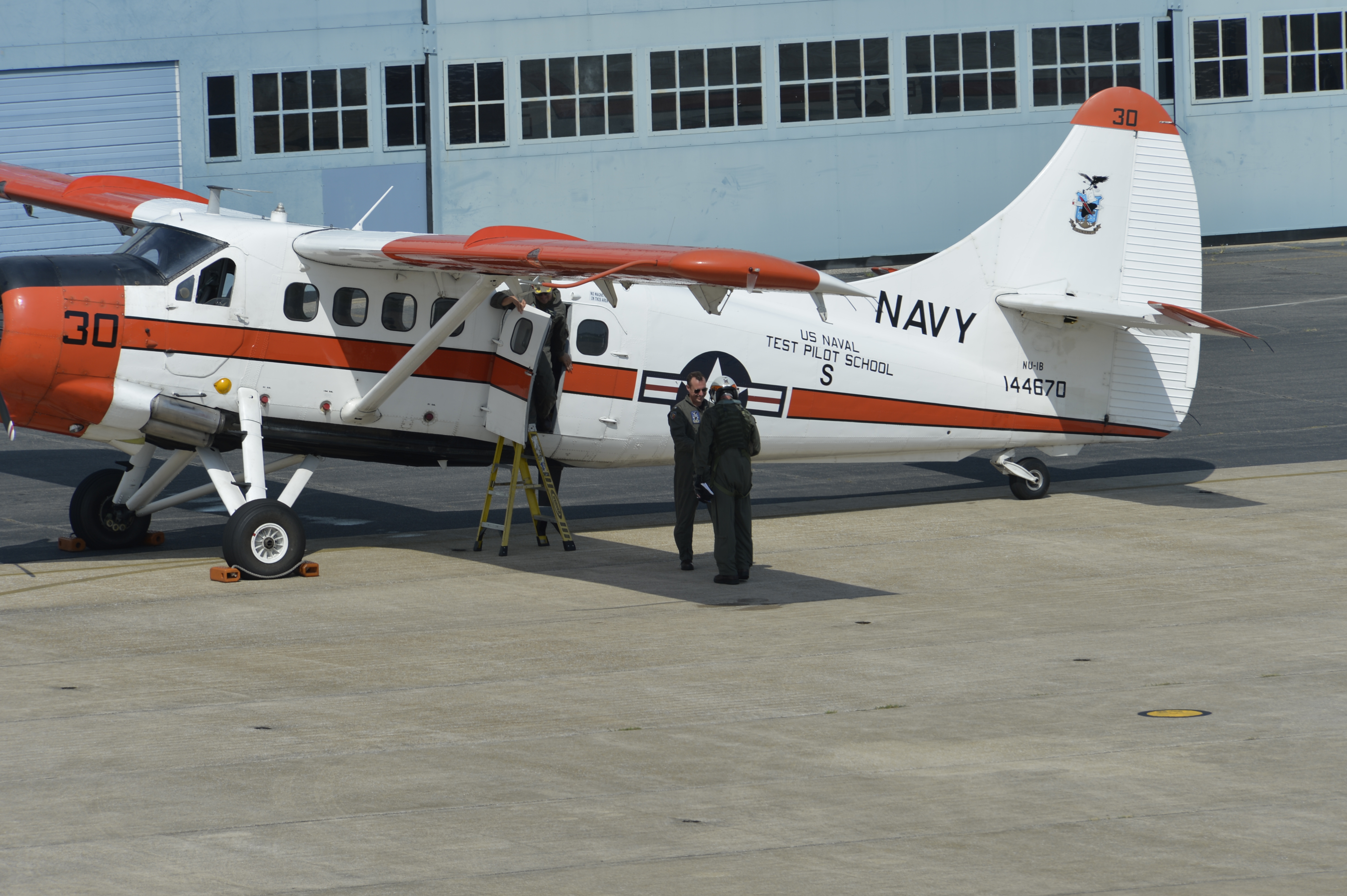 Cmdr. Jeremy DeBons shakes hands with Lt. Col. Rory Feely in front of the school's NU-1B Otter aircraft.