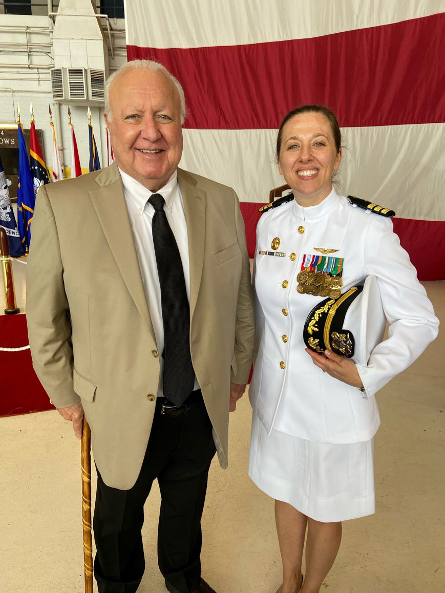 A man in a khaki blazer standing with a woman naval officer in Navy dress whites