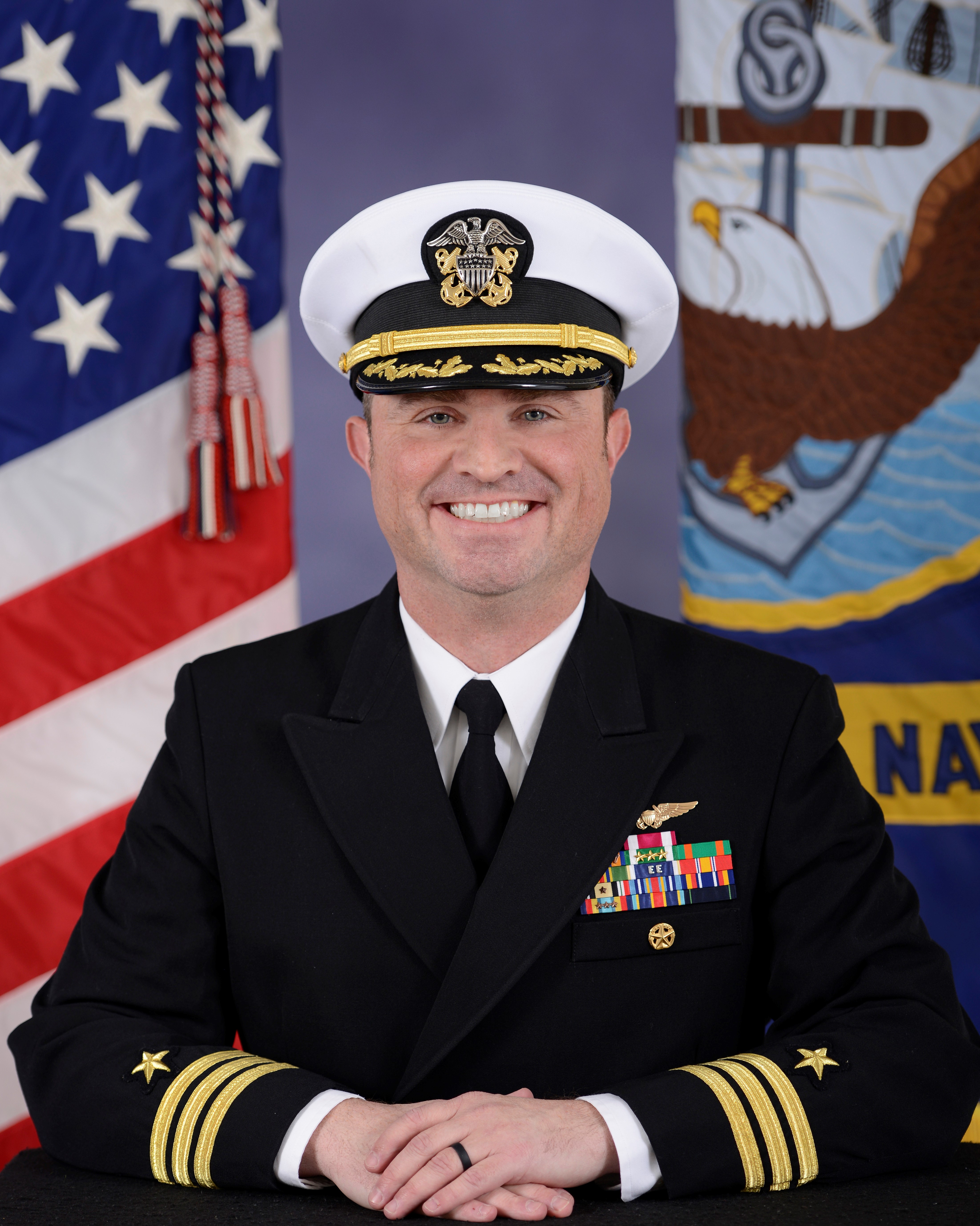 Man in front of the US Navy and American Flags Wearing a Navy Captain Uniform