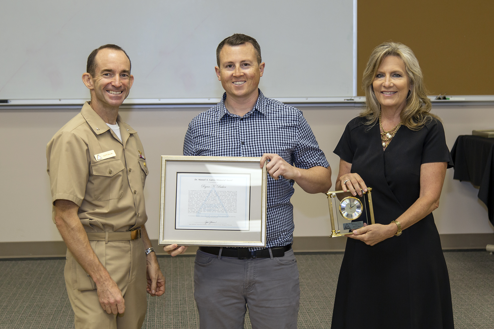 Rear Adm. Scott Dillon, left, NAWCWD commander, and Joan Johnson, right, NAWCWD executive director, pose with Dr. Manuel A. Garcia Memorial Award winner Ryan Baker during the Honorary Awards Ceremony in Point Mugu, California, on June 27. Award recipient James Bender was unable to attend. (U.S. Navy photo by Rob Grabendike)