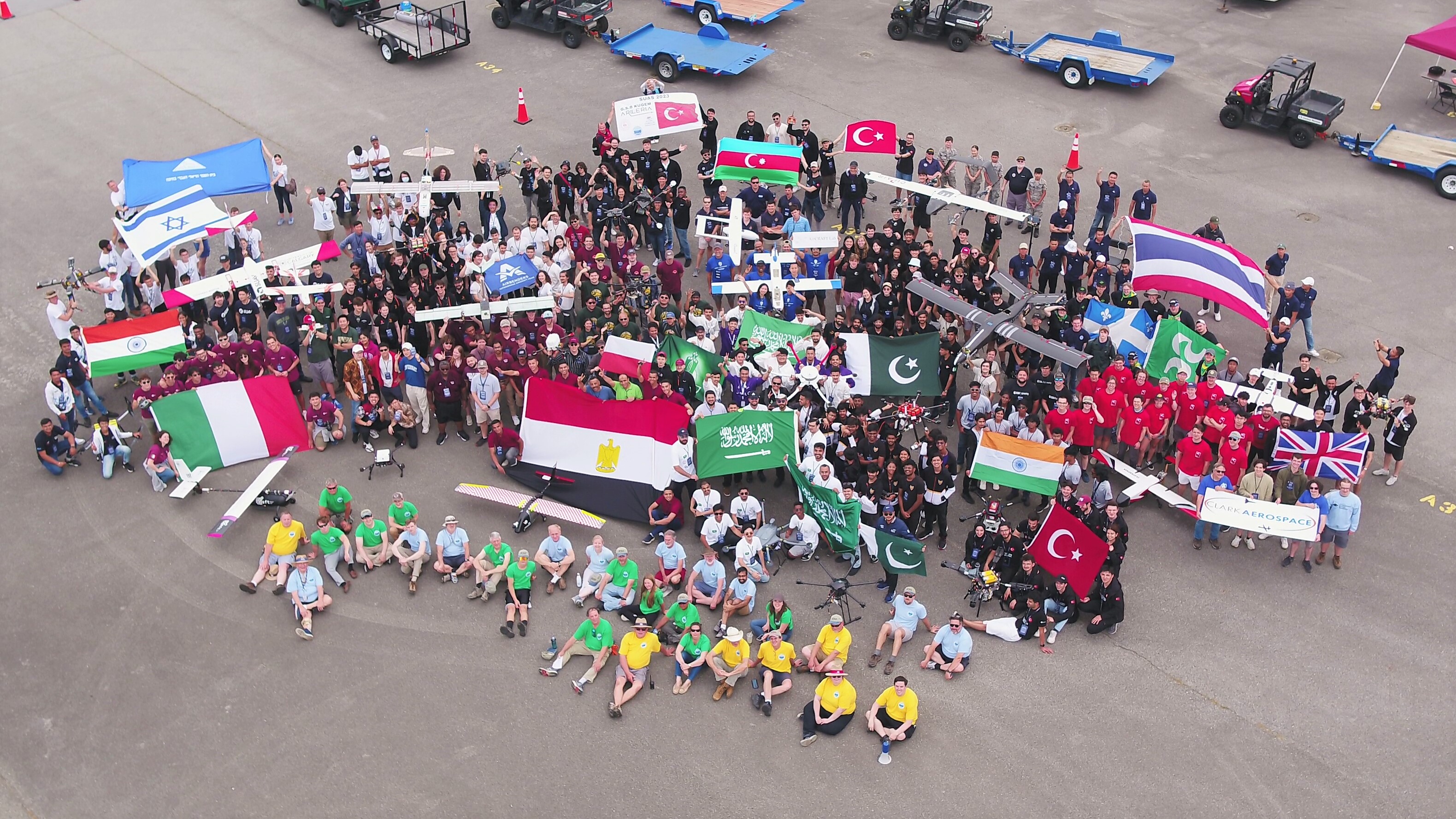 Dozens of students gather for a photo on a flight line posing with small unmanned systems and their home country flags.