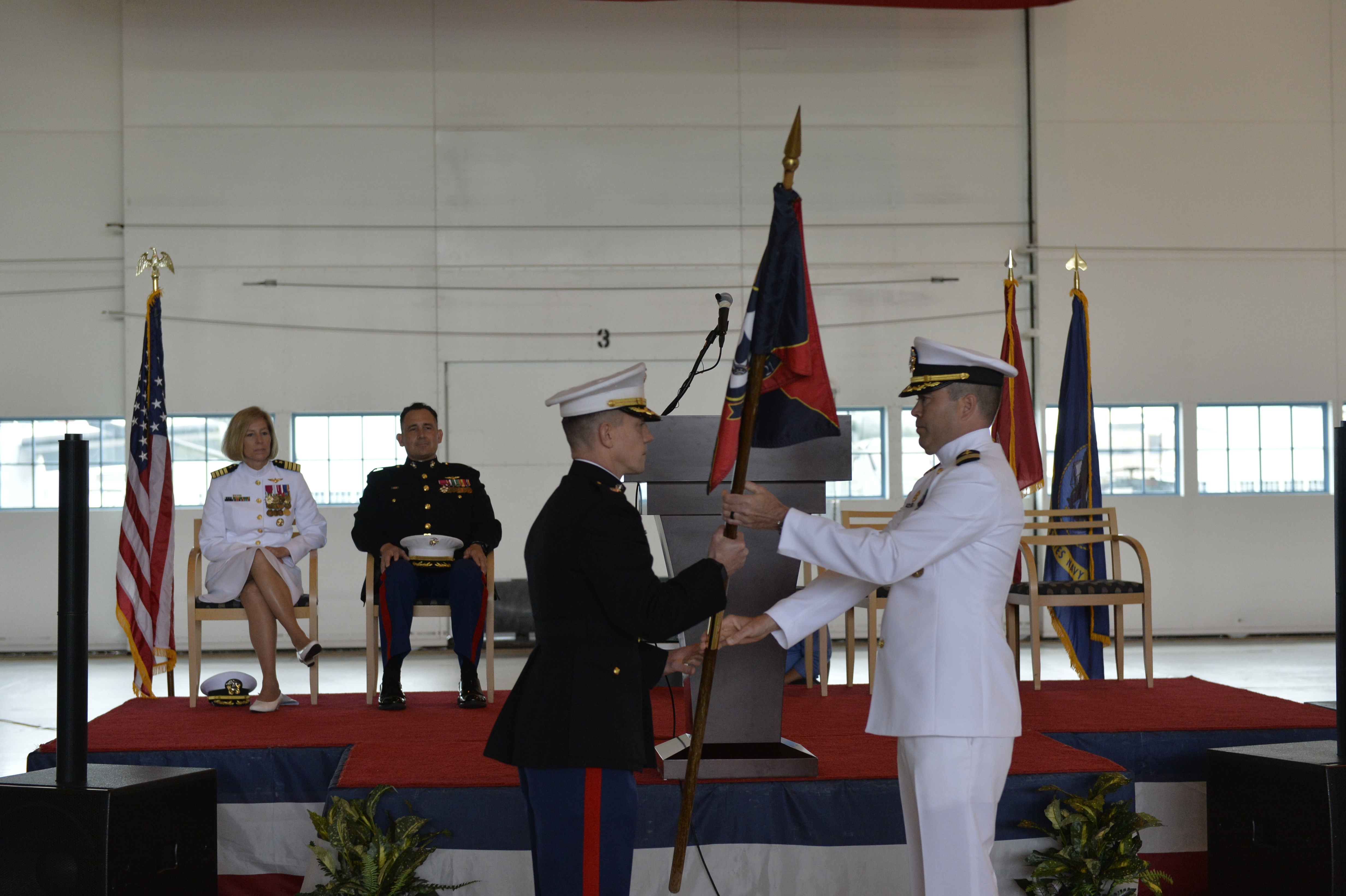 Lt. Col. Matthew Baumann takes a command flag from Cmdr. Daniel short in an aircraft hangar.