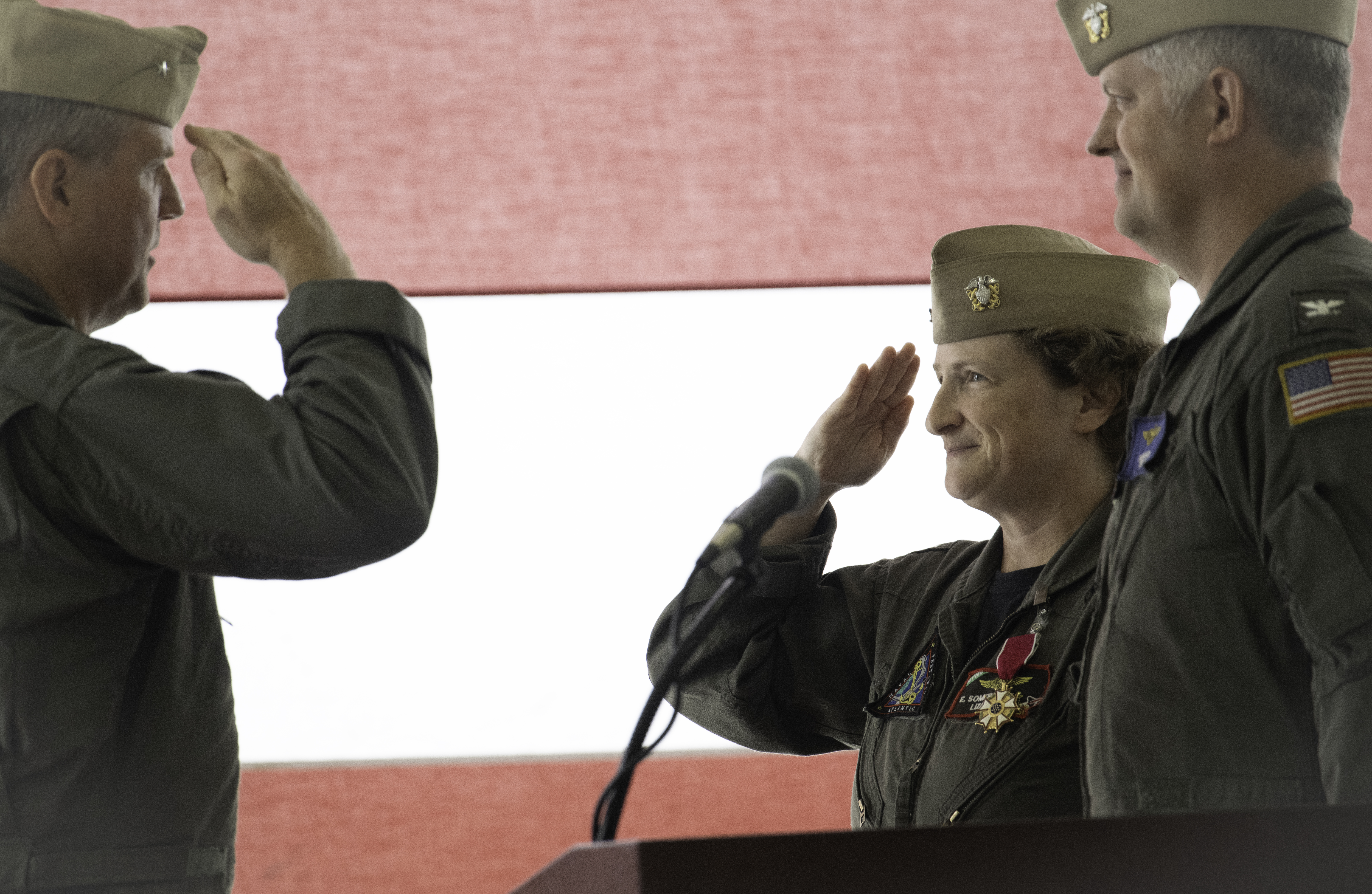 Rear Adm. Evans salutes Capt. Somerville in front of a flag at the podium during the Naval Test Wing Atlantic change of command.