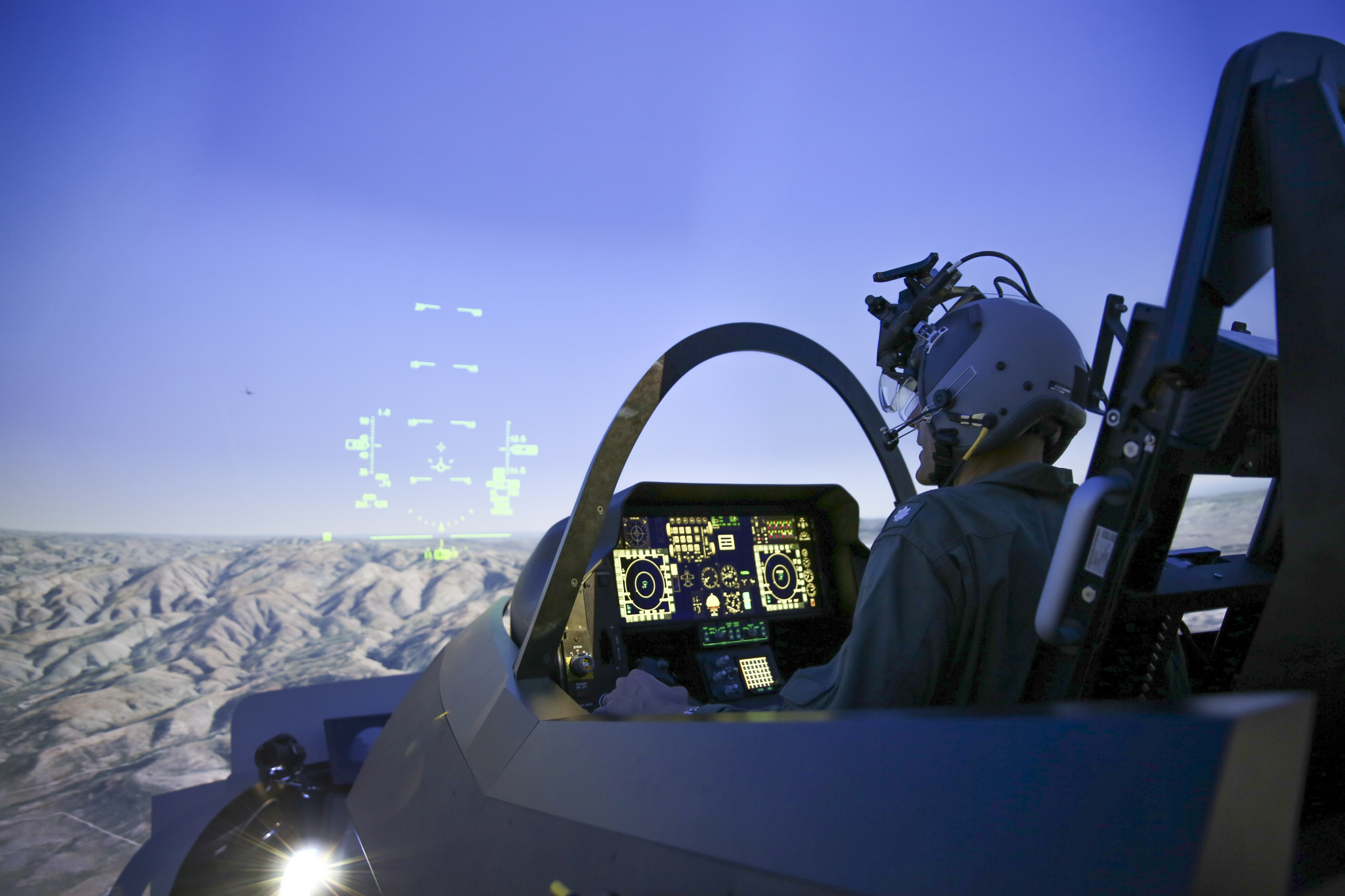 A pilot operates a fighter jet cockpit in a domed simulator.